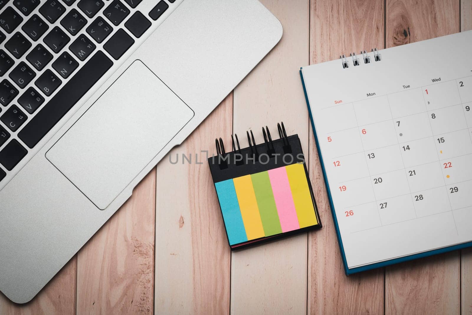 A laptop, index flag, and calendar are neatly placed on the wooden desk for efficient workspace organization