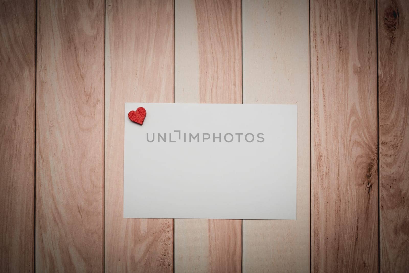 A conceptual white paper adorned with a love-themed red heart on a wooden table for Valentine's Day