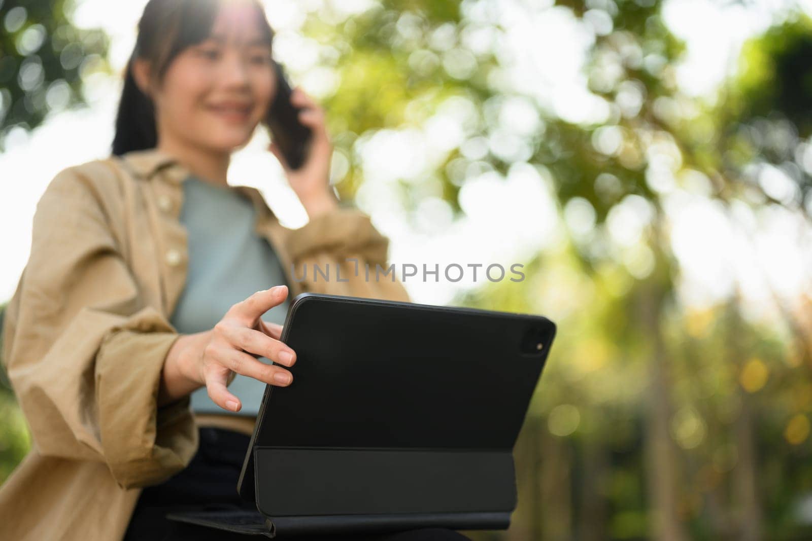 Cropped shot young woman using digital table and talking on mobile phone at outdoor.