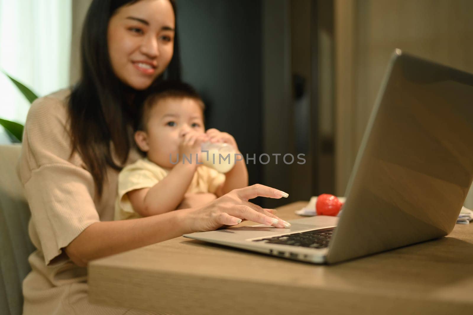 Cropped shot mother working with laptop at home with little baby son. Motherhood and child care concept by prathanchorruangsak