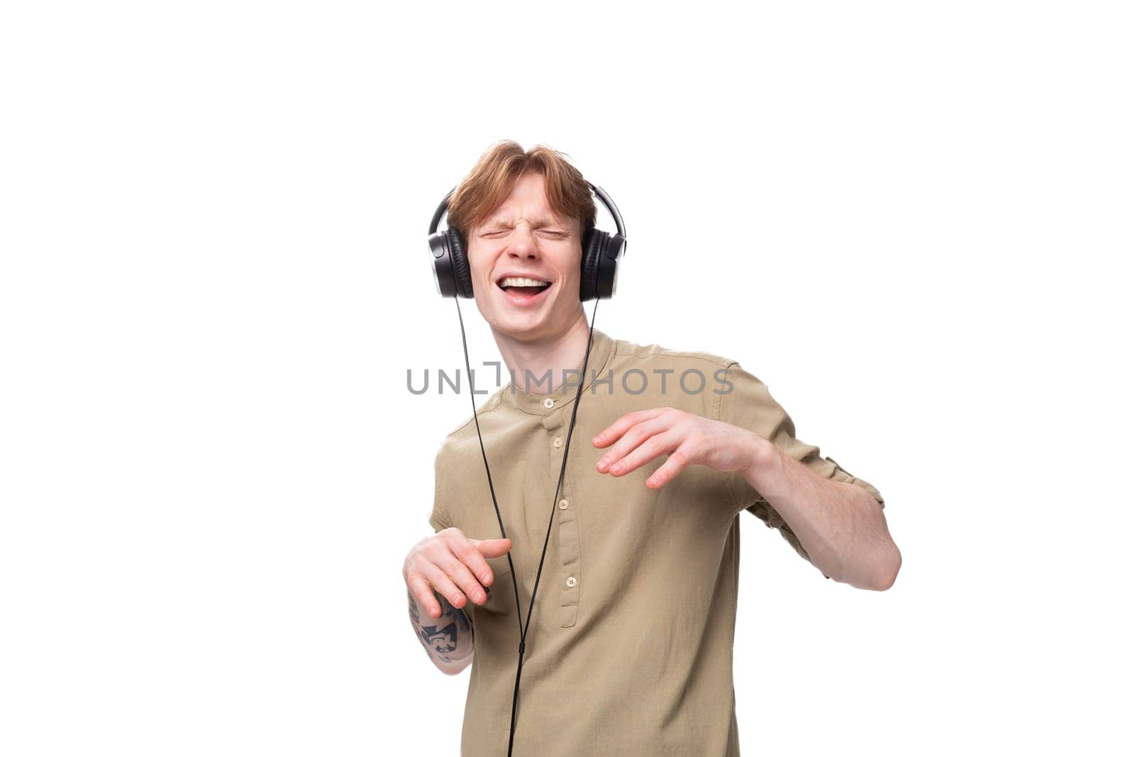 young handsome red-haired student man dancing to the music in large wired headphones.