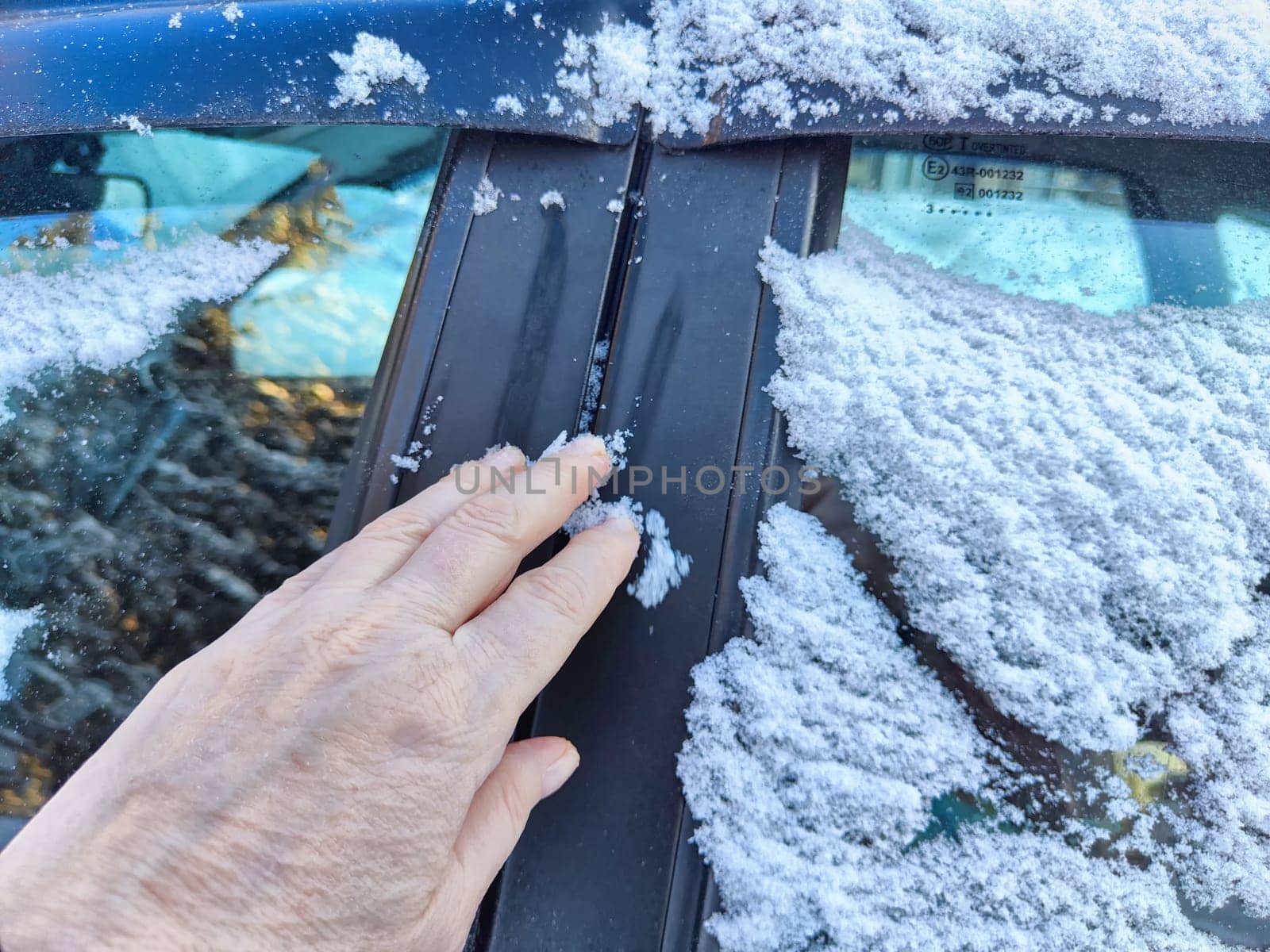 Hand of Woman persons brushing snow of car window, which frozen over during a bitterly cold morning. Problem with travel and trip in winter