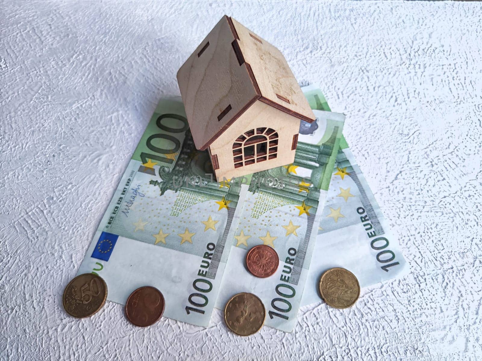 Miniature house placed atop European currency, indicating real estate investment or savings. Wooden Miniature House on Euro Banknotes and Coins