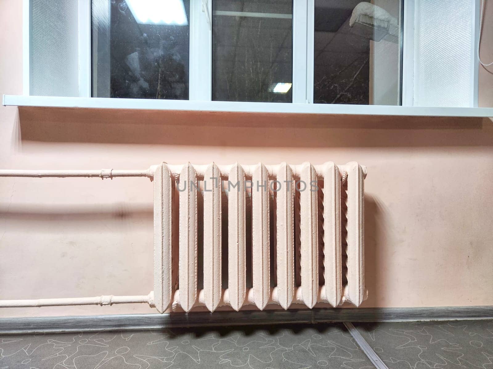 A classic radiator sits below a window in room with pink walls. Vintage Radiator Against Pink Wall Under Window at Night