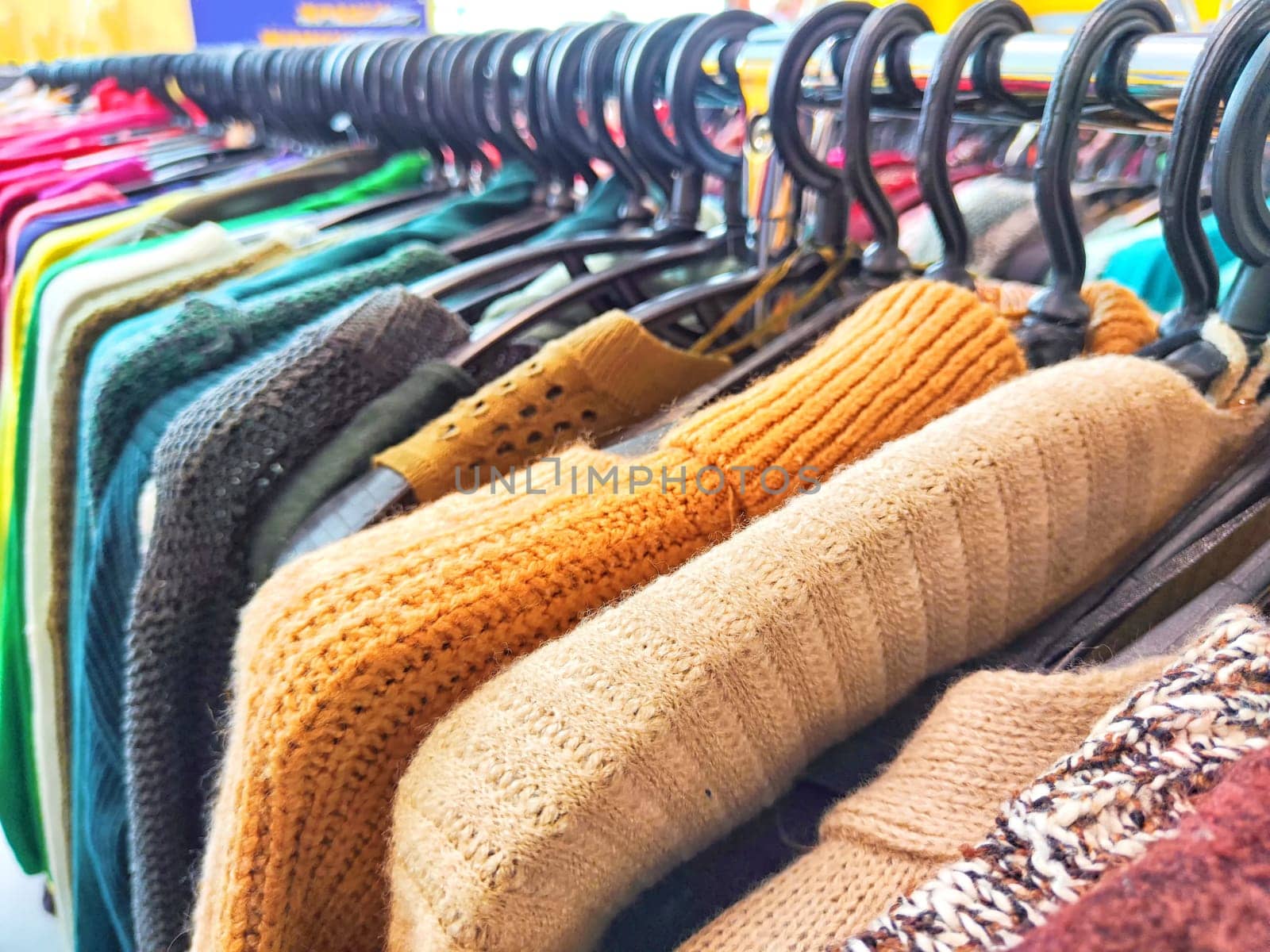 Colorful Assortment of Knitted Sweaters on Display in Bright Clothing Store. Variety of colorful sweaters hanging on a rack in a shop