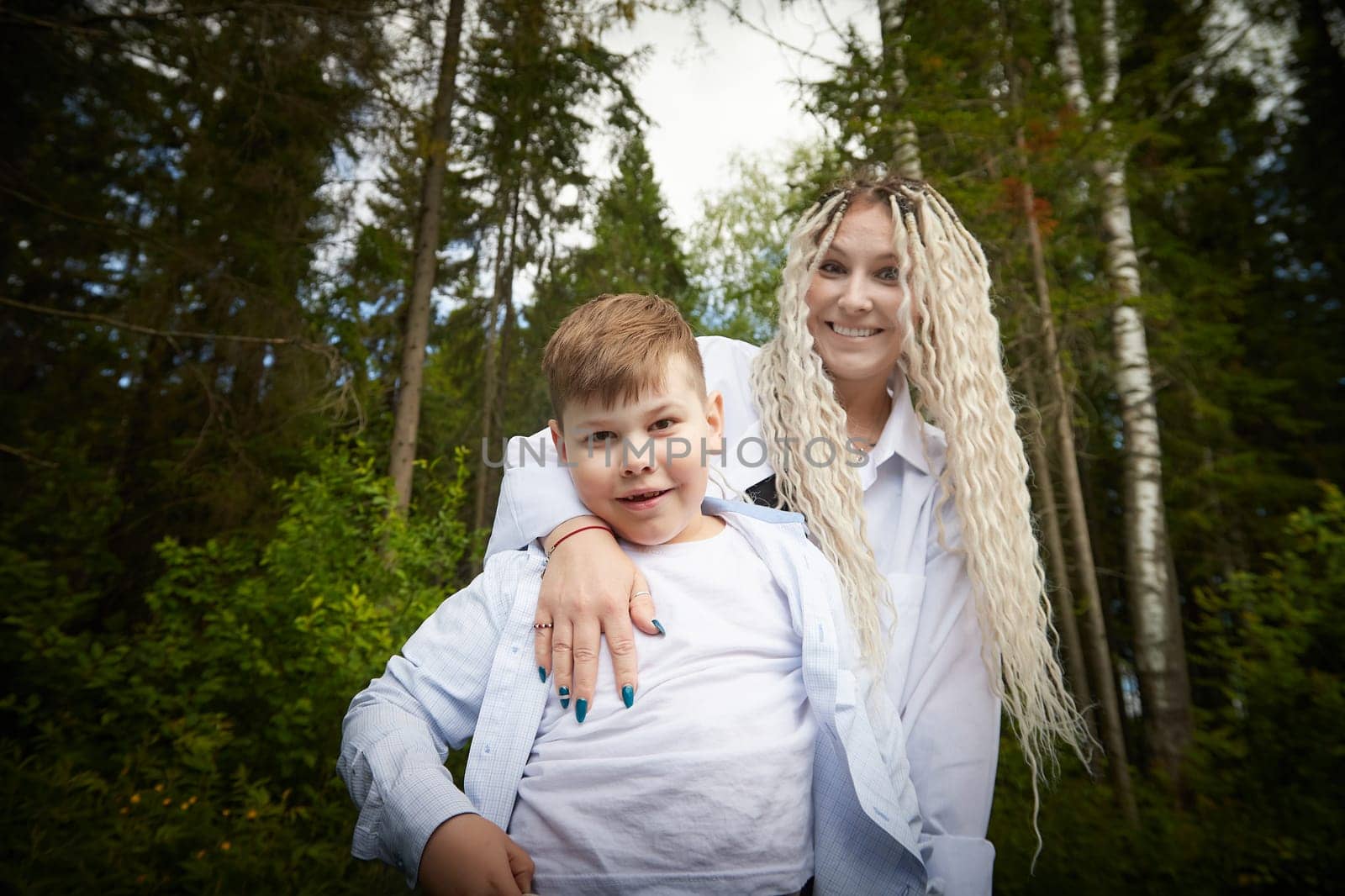 Funny mother with dreadlocks and fat boy happy hugging in forest on a sunny summer day
