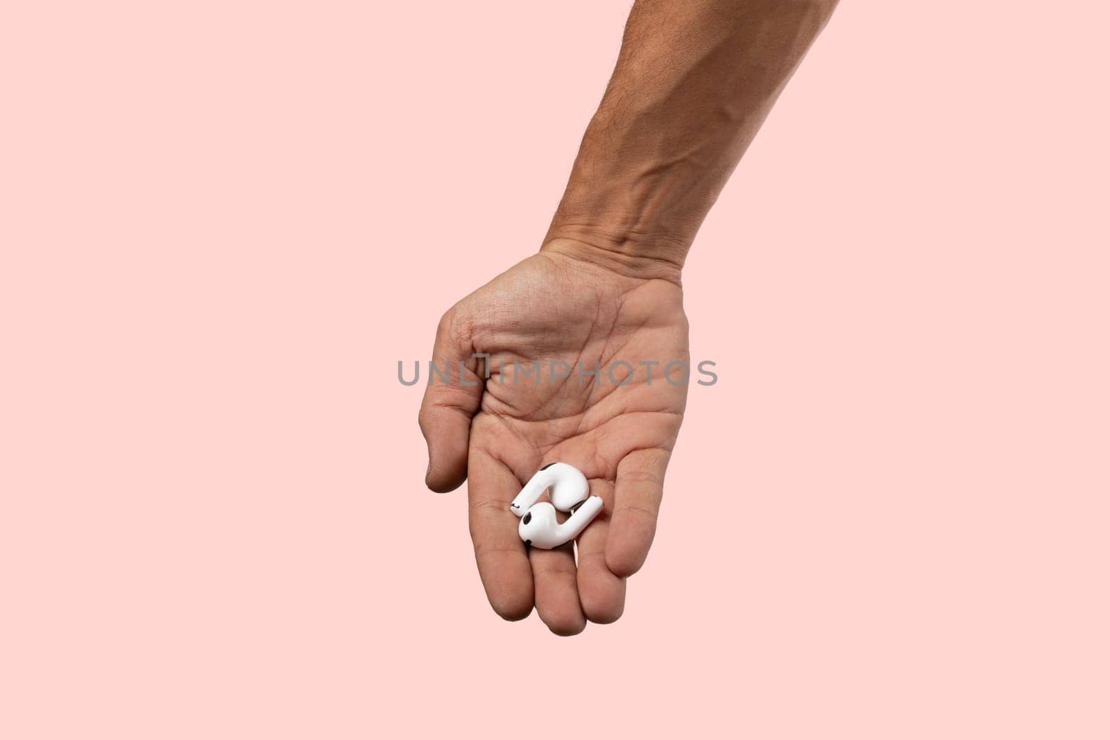 Male hand holding white earbuds on pink background. High quality photo