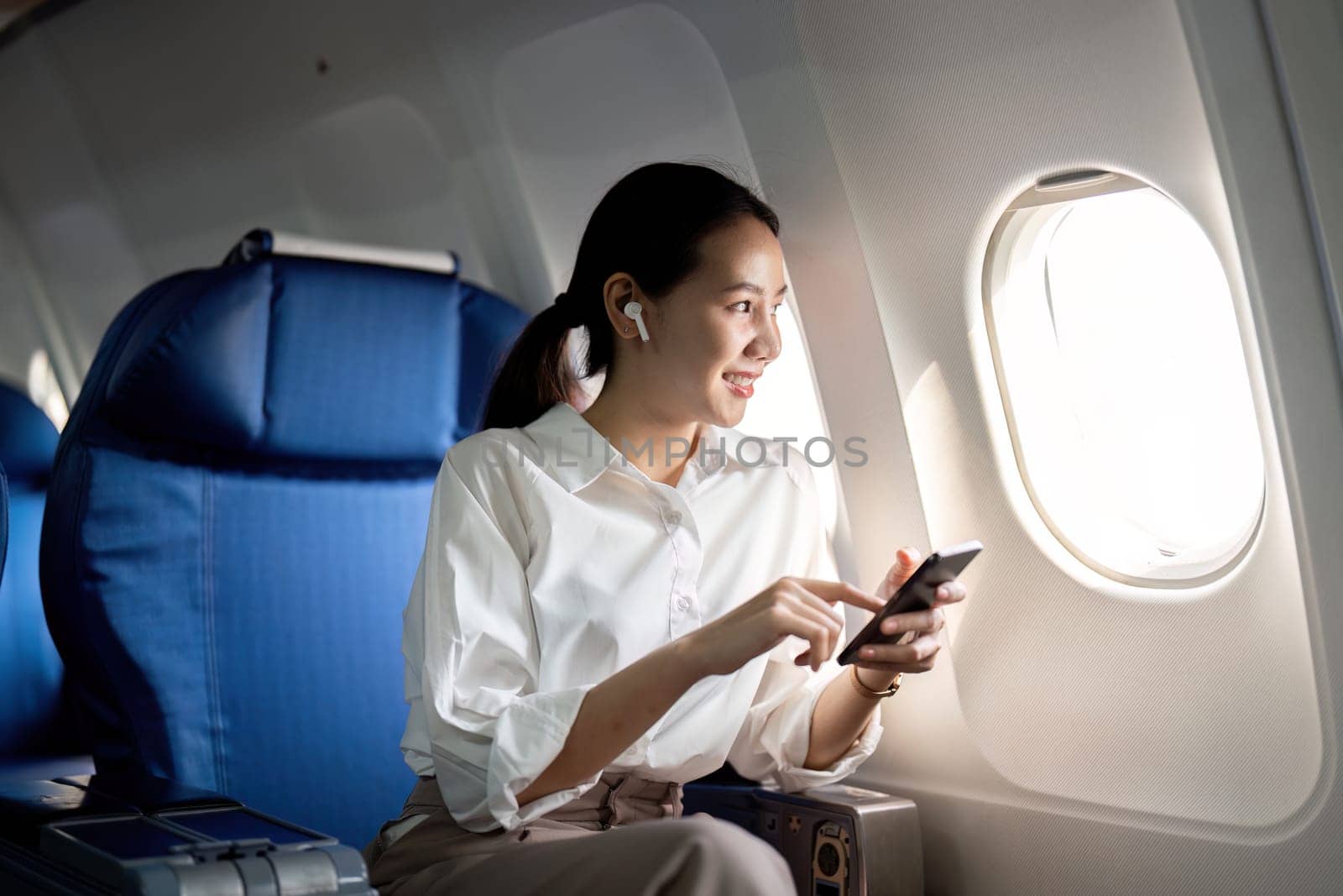 Traveling and technology. Flying at first class. Young business woman passenger using smartphone while sitting in airplane flight by nateemee