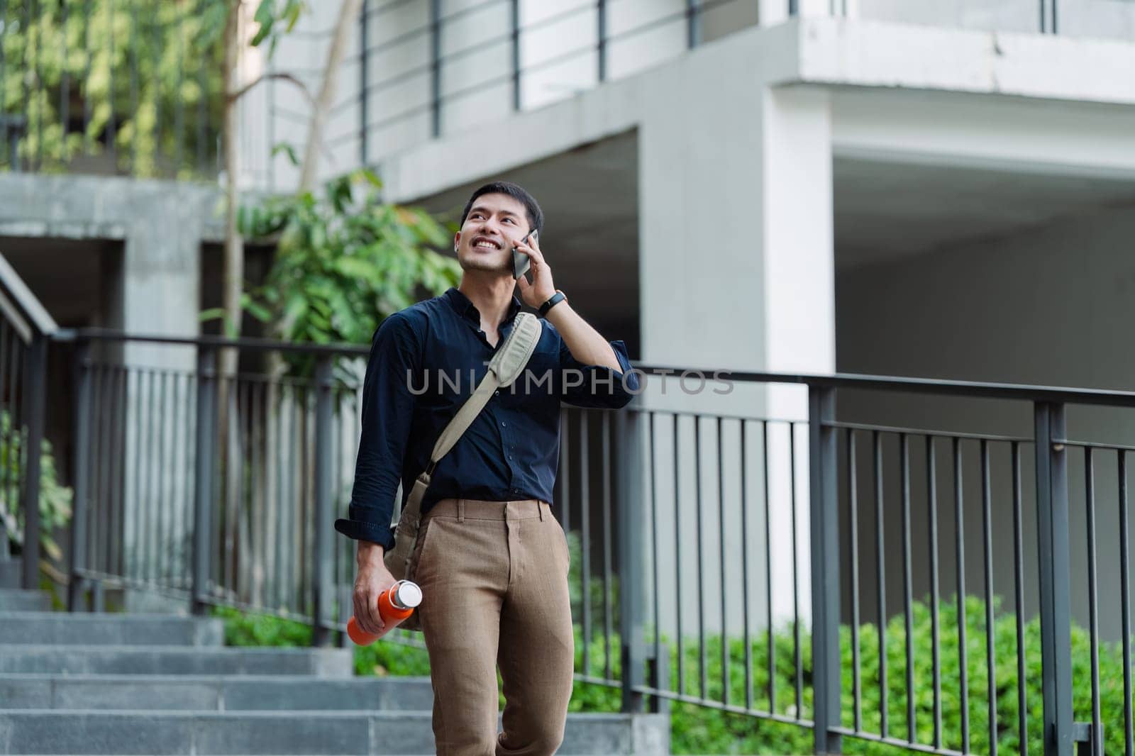 Smiling asian businessman hold reusable eco-friendly ecological cup and using mobile while on the way home at park by itchaznong