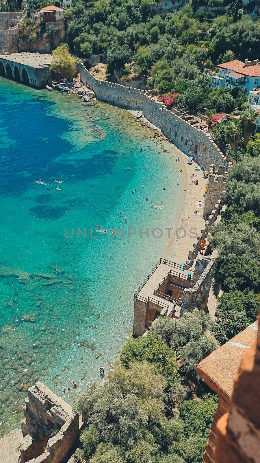 Top view of azure sea, sandy beach with people along walls of old castle. concept of beach holiday, summer vacation. vertical photo by Leoschka