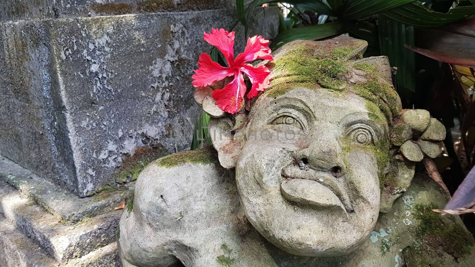 Beautiful artistic Bali stone statue of a Balinese ancient garden statue used as garden decoration, javanese gnome indonesia along with plants and flower