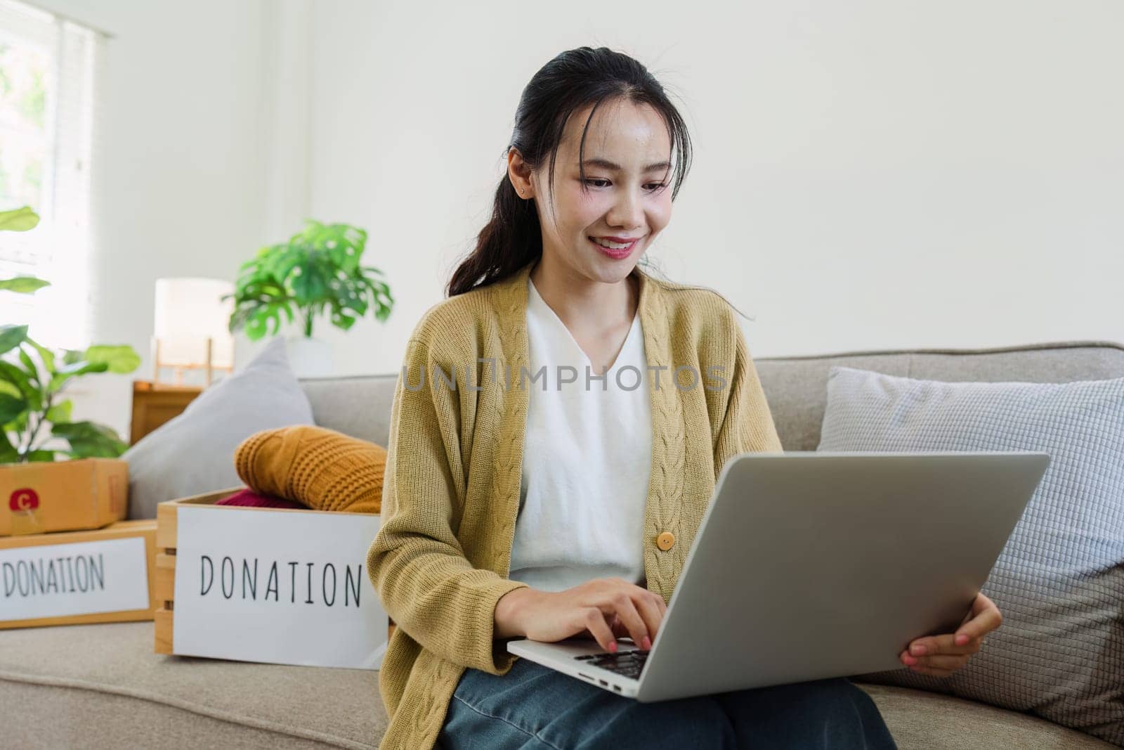 Asian young woman using laptop for donate box with second hand clothes by itchaznong
