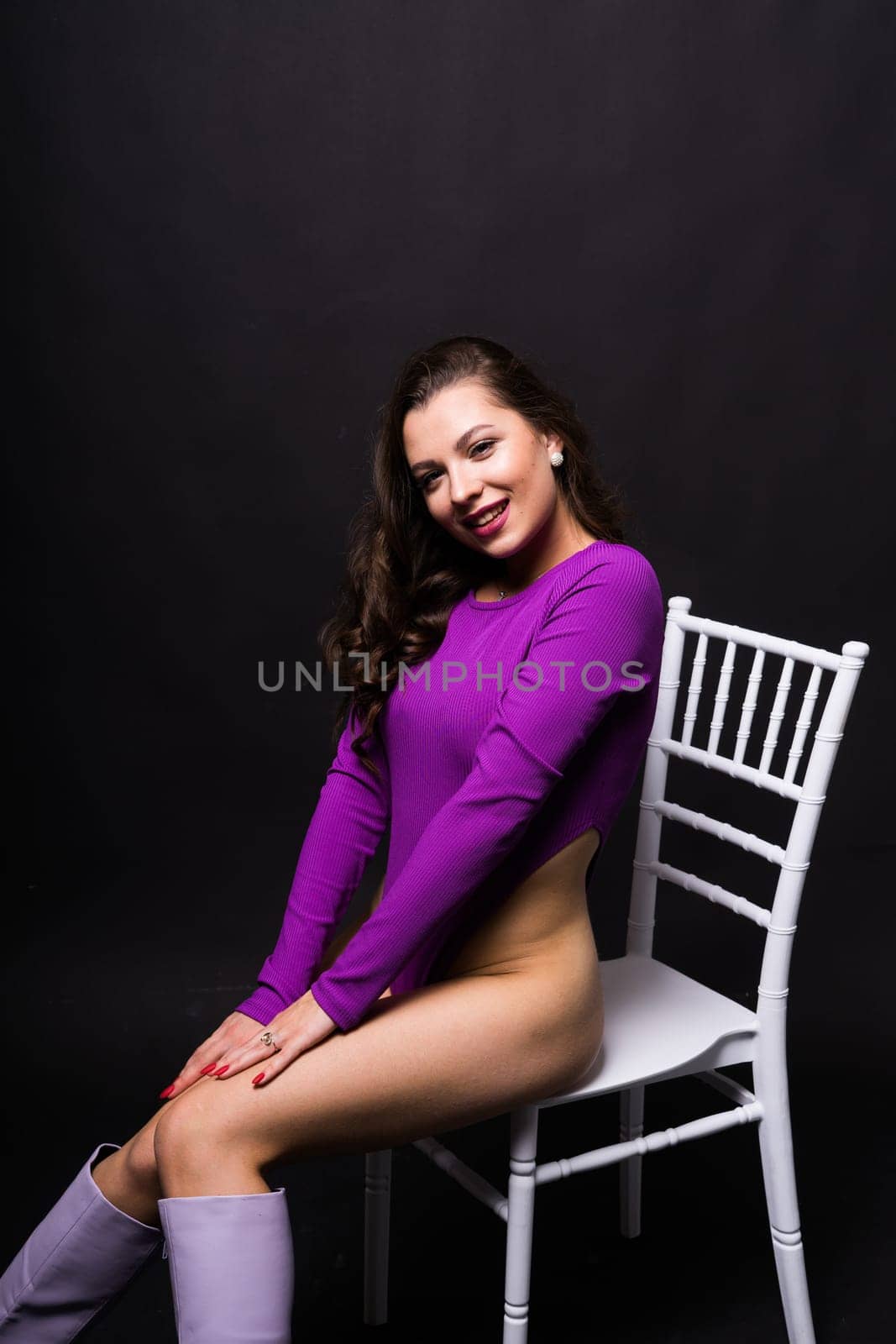 Slender seductive brunette female in violet bodysuit against a dark background.