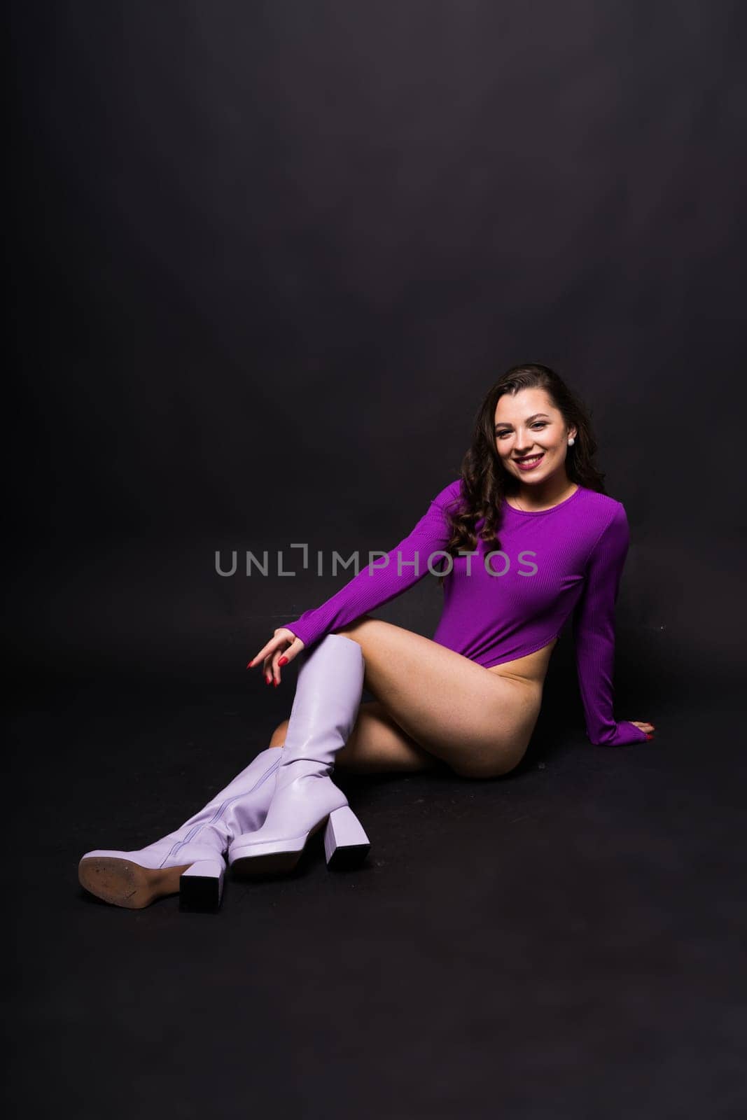 Slender seductive brunette female in a violet bodysuit against a dark background. by Zelenin