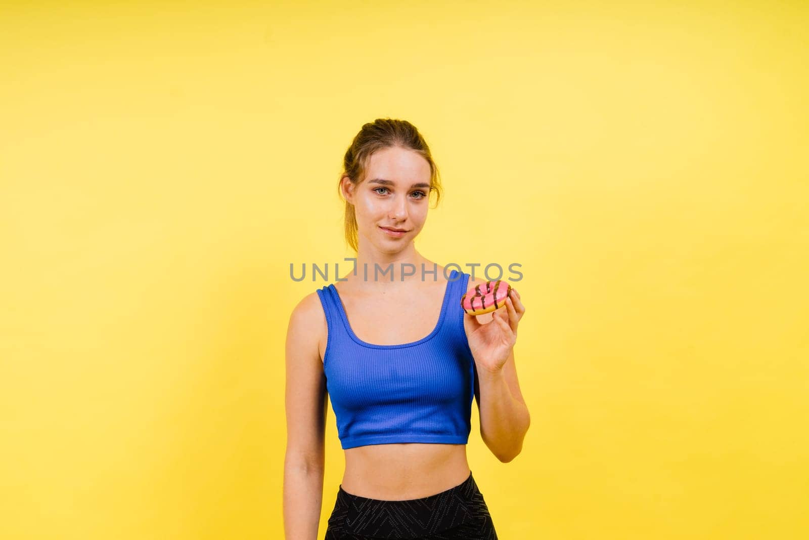 Young cute sport woman eating a donut cake in studio background by Zelenin