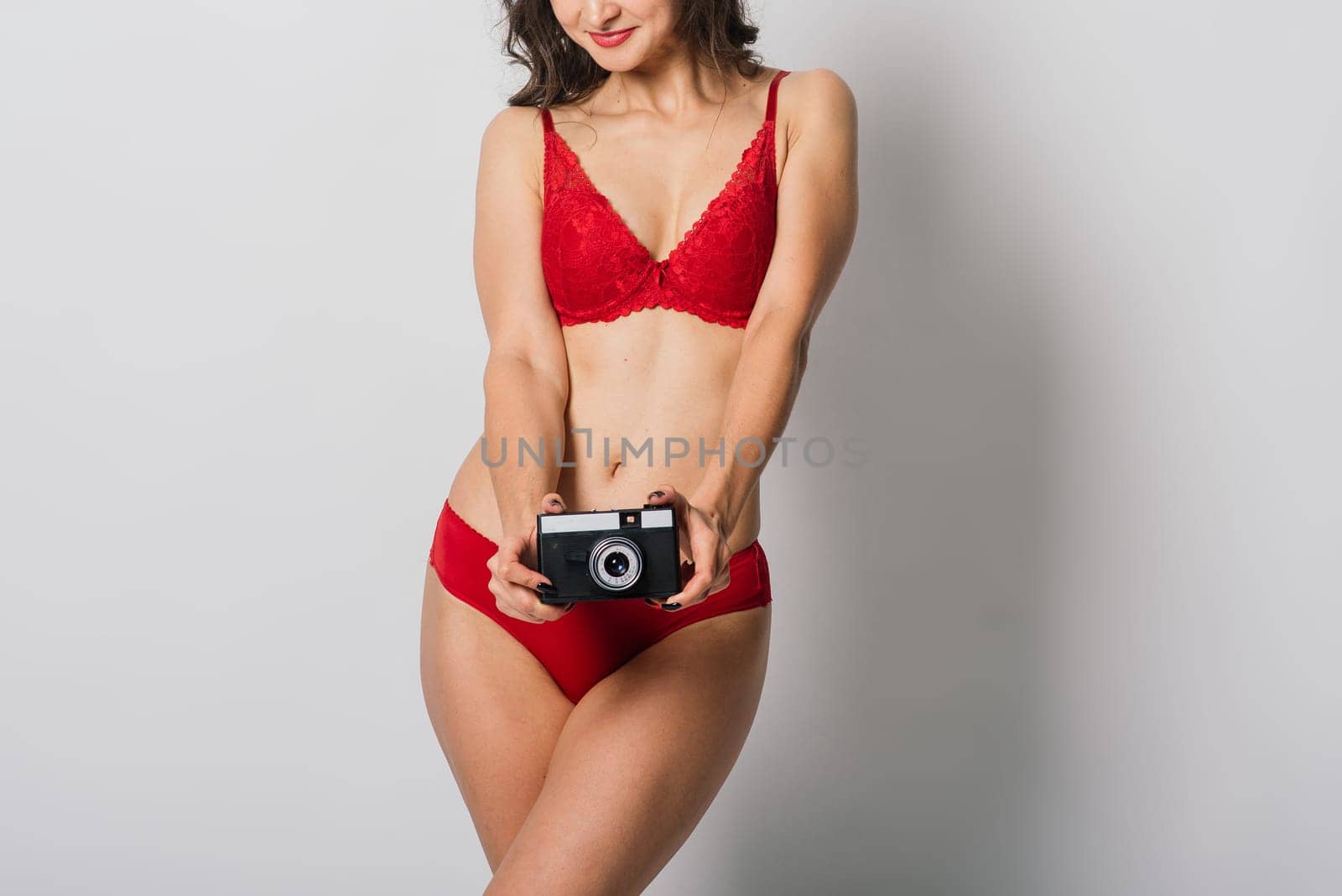 Beautiful female with pretty smile in red lingerie holding photo camera, isolated on white by Zelenin