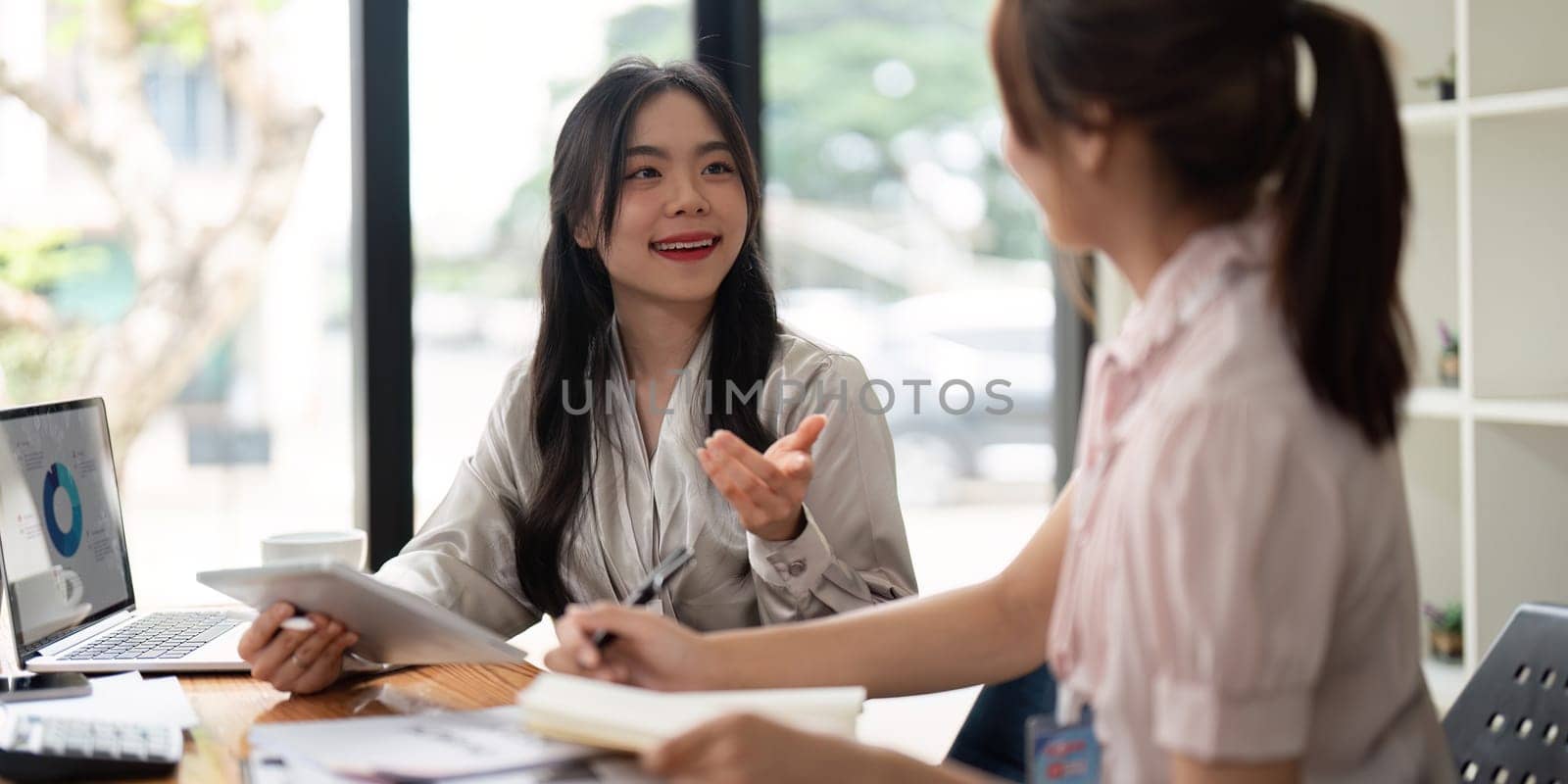 Two Asian businesswoman working with laptop computer and discussing documents and idea at meeting. Teamwork process.
