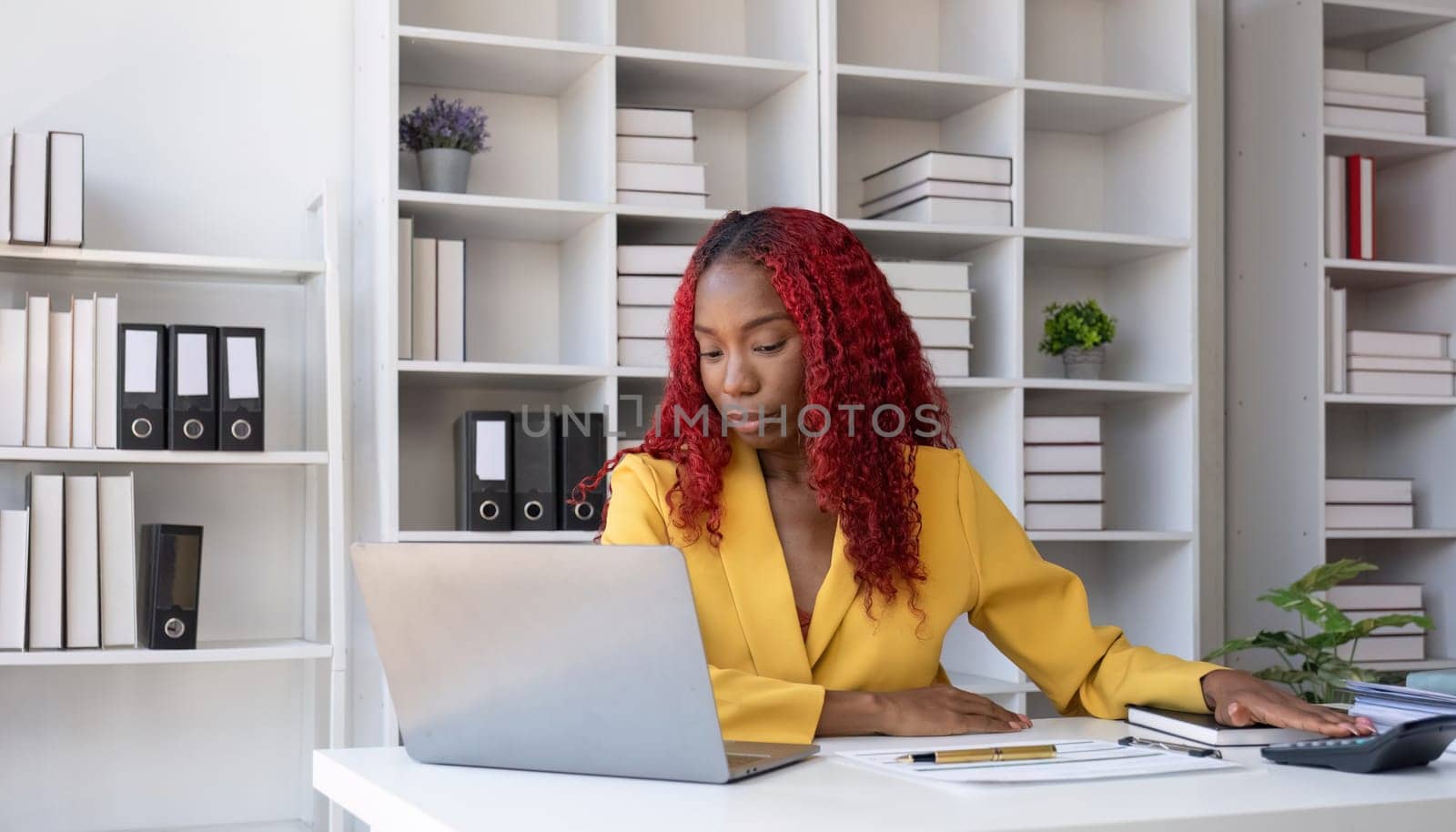 African American businesswoman is unhappy sitting on her office desk doing accounting and finance work. by wichayada