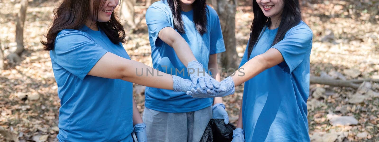 A group of Asian volunteers joined hands before helping to collect trash in plastic bags and clean areas in the forest to preserve the natural ecosystem. by wichayada