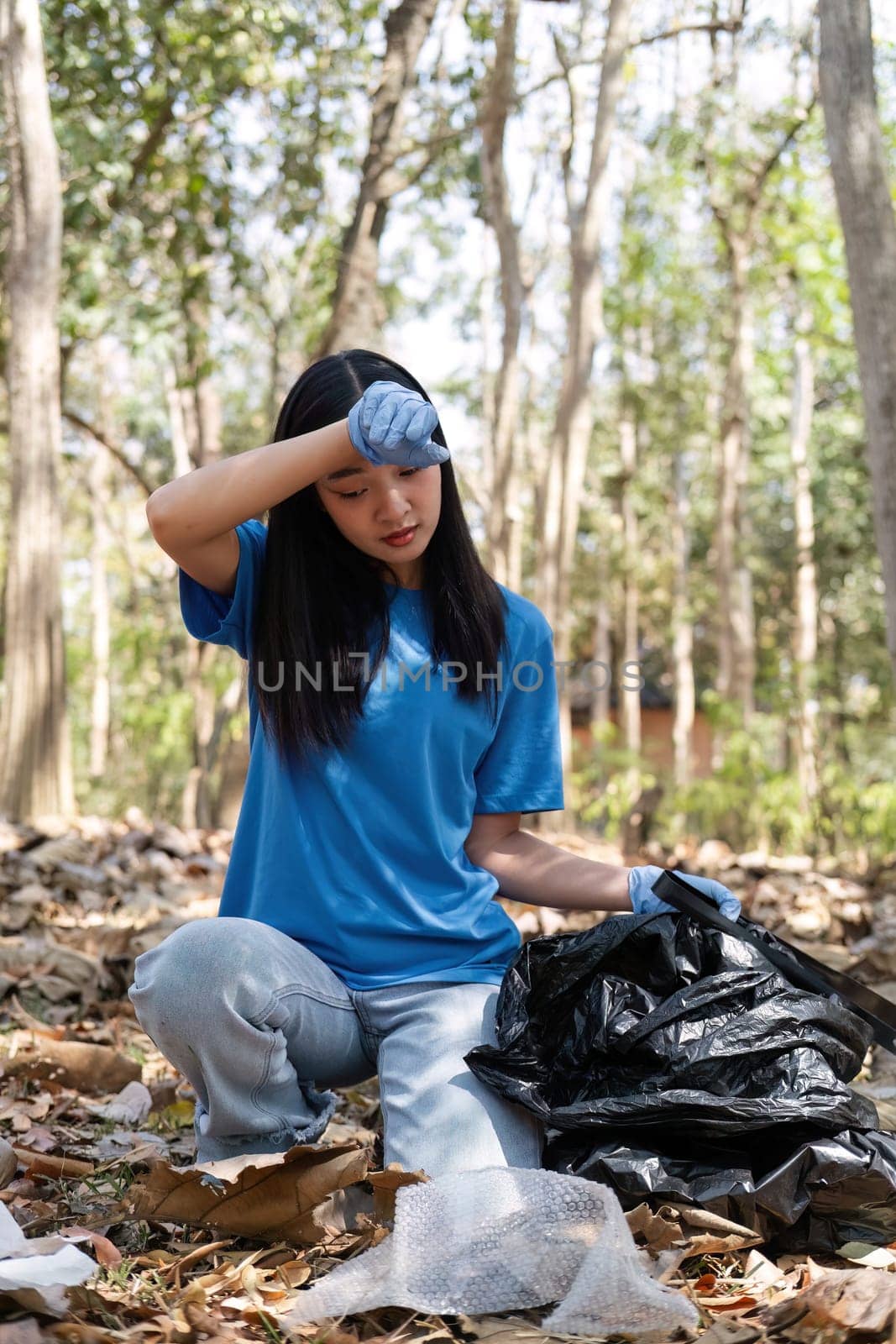 young woman holds a garbage bag and a group of Asian volunteers collect garbage in plastic bags and clean up