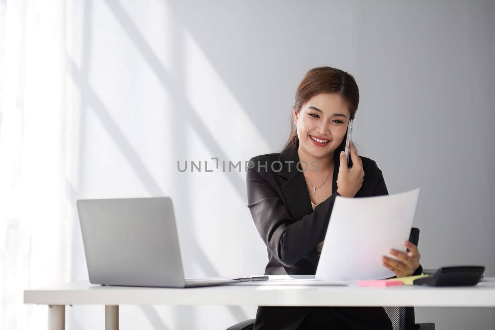 Businesswoman using laptop and mobile phone talking about work and managing company business by wichayada