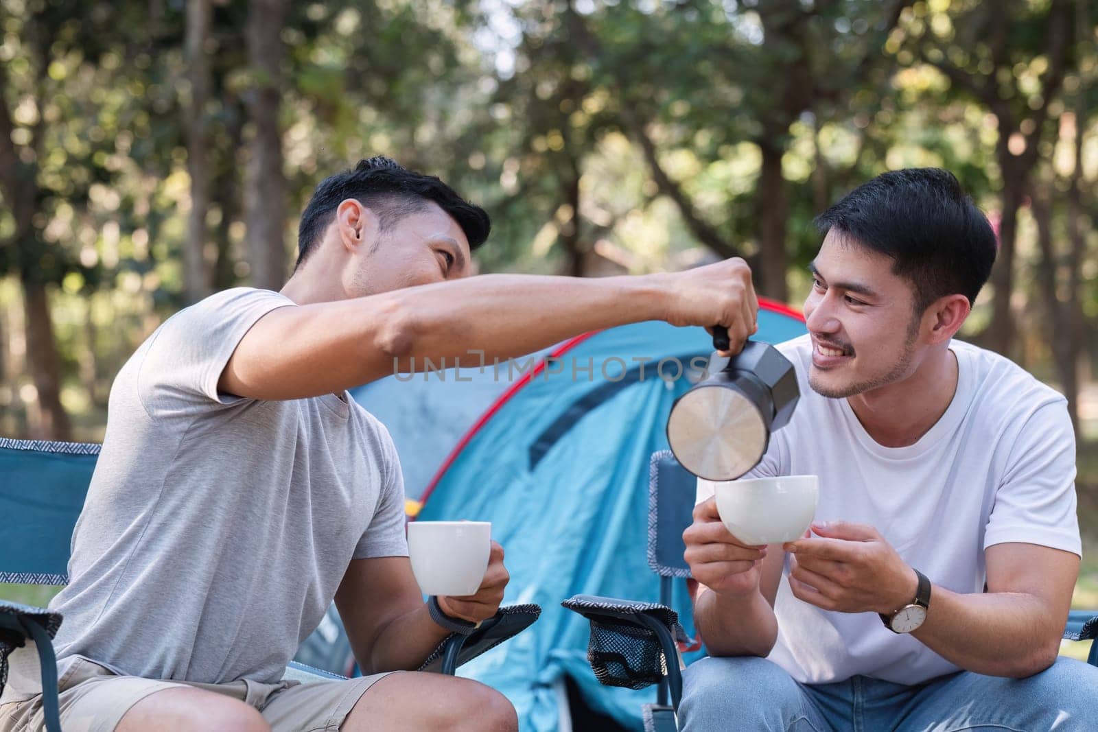 Asian LGBTQ couple drinking coffee in a romantic camping tent. LGBTQ couple drinking coffee in a camping tent, enjoying nature, forest, camping atmosphere, LGBTQ, gay, gay men..