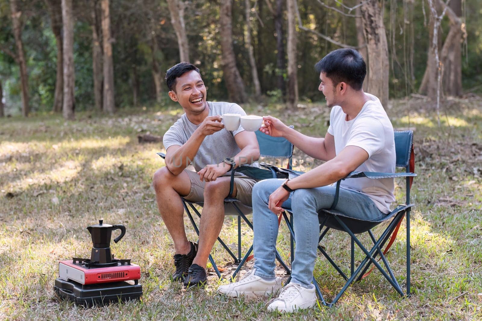 Asian LGBTQ couple drinking coffee in a romantic camping tent. LGBTQ couple drinking coffee in a camping tent, enjoying nature, forest, camping atmosphere, LGBTQ, gay, gay men. by wichayada