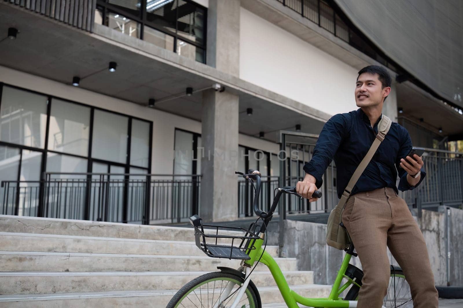 A young Asian businessman rides a bicycle to work. Standing outside the office talking on the phone and talking about business. Concept of reducing energy and reducing air pollution. by wichayada
