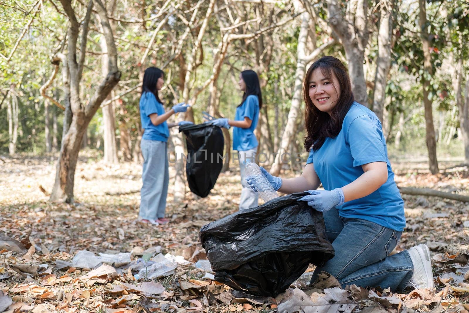 A group of Asian volunteers collects trash in plastic bags and cleaning areas in the forest to preserve the natural ecosystem..