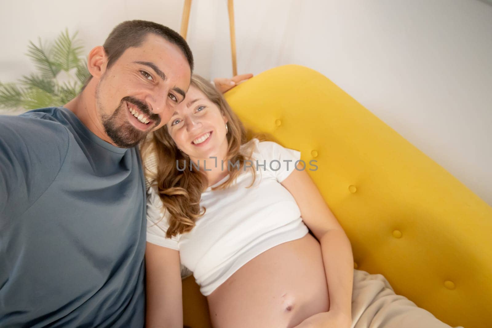 A pregnant woman and her husband are photographing themselves on the cell phone at home. by PaulCarr