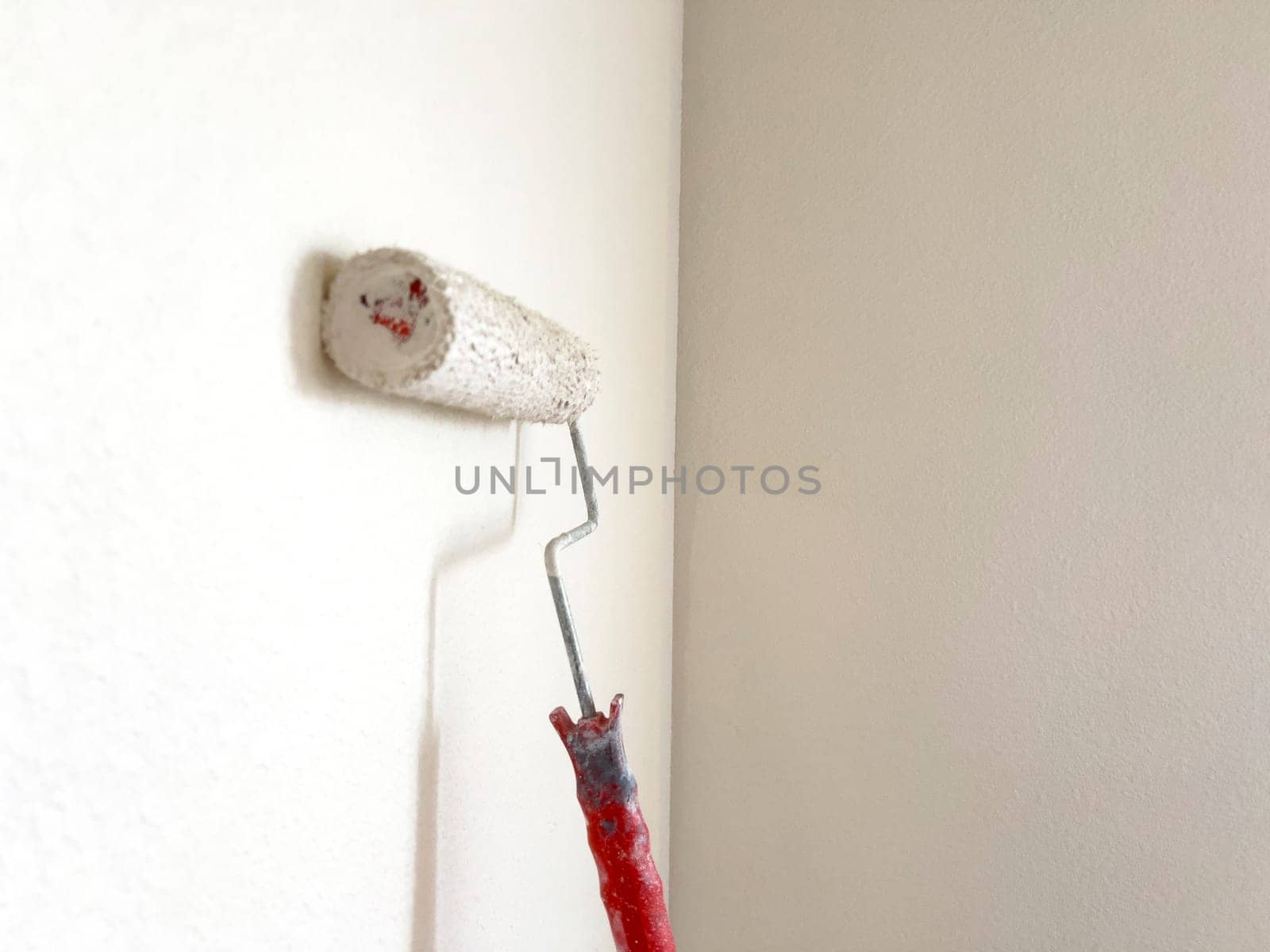 Detailed process of painting a wall, with a focus on a paint roller applying a fresh white coat, symbolizing the transformative power of a simple home improvement task.