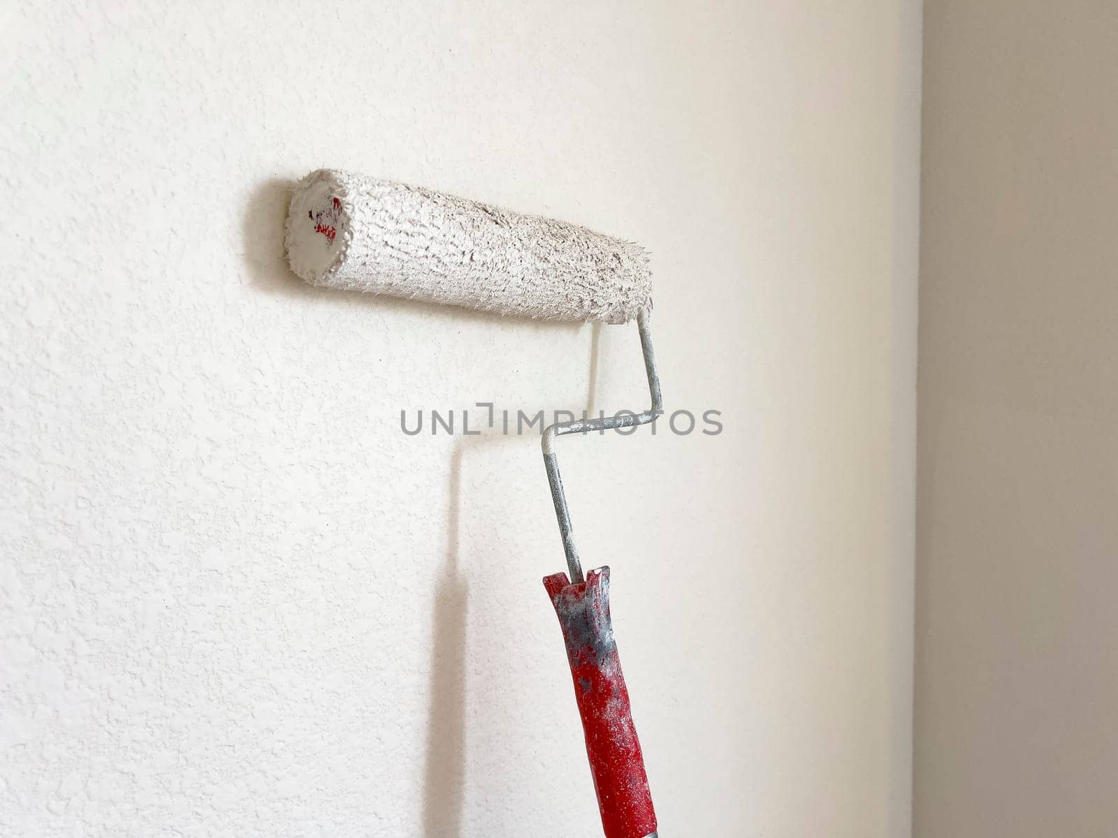 Detailed process of painting a wall, with a focus on a paint roller applying a fresh white coat, symbolizing the transformative power of a simple home improvement task.