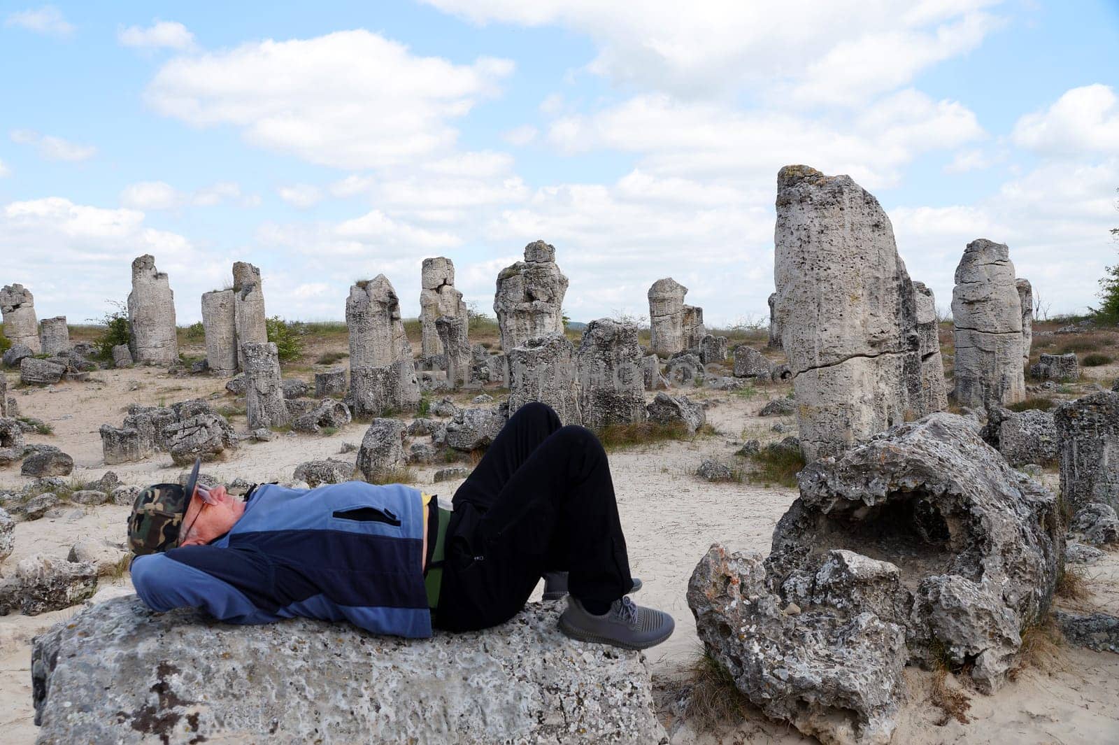 a lonely tourist rests on a stone in a historical open-air museum among ancient stone pillars.