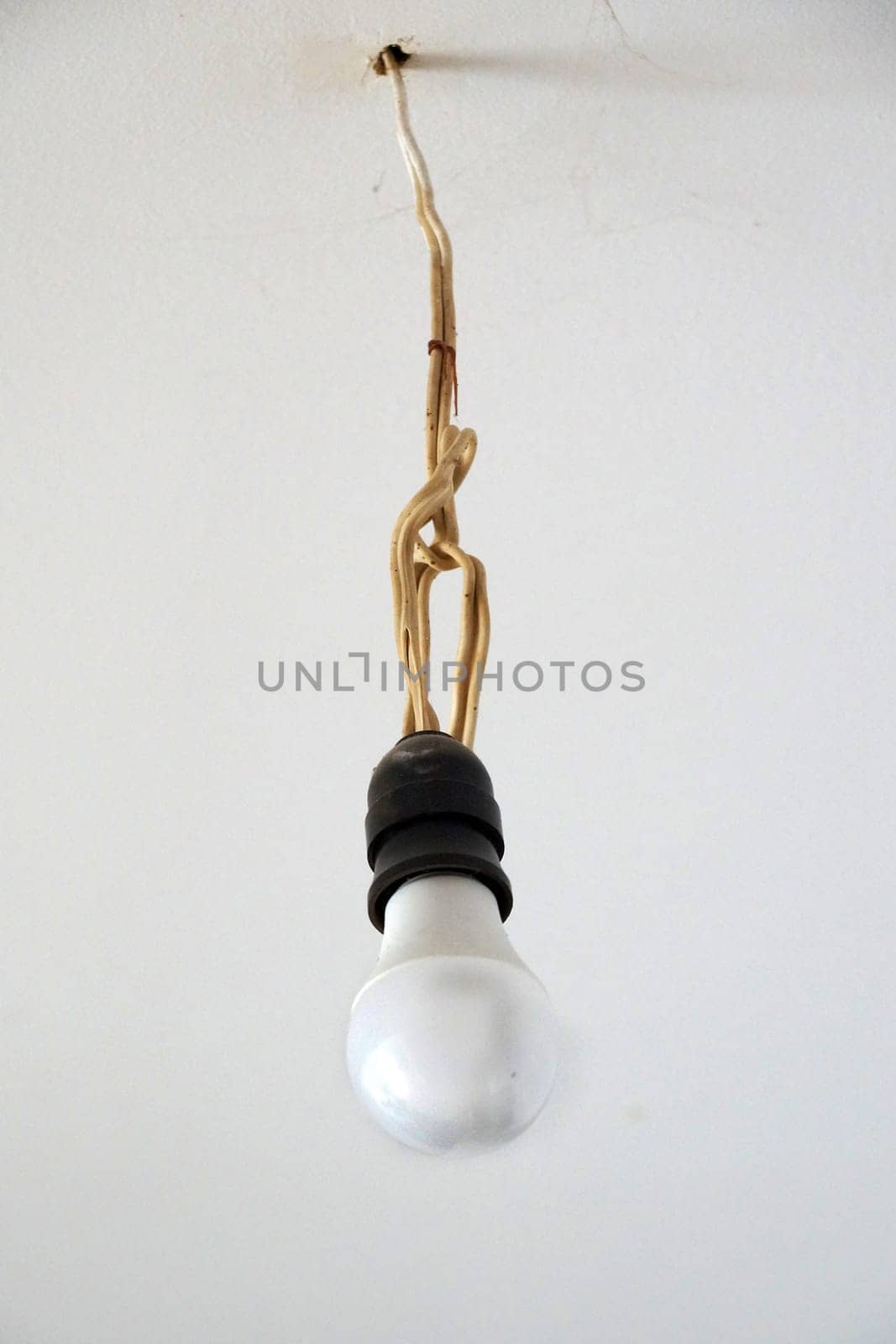 energy saving light bulb on an old wire hanging on the ceiling by Annado