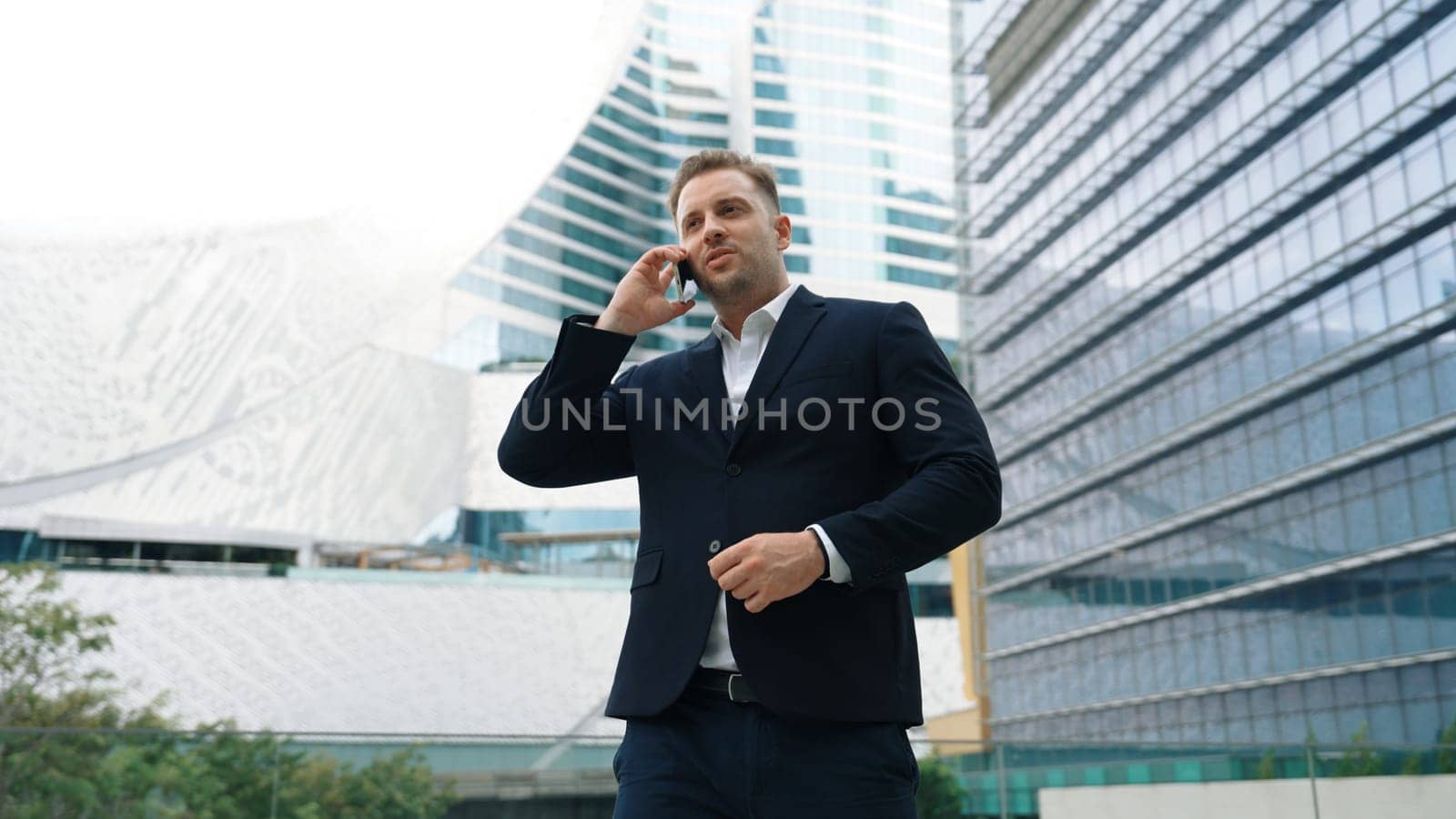 Skilled businessman talking to marketing team about marketing strategy by using phone while standing at skyscraper. Happy manager calling colleague about increasing sales at modern urban city. Urbane.