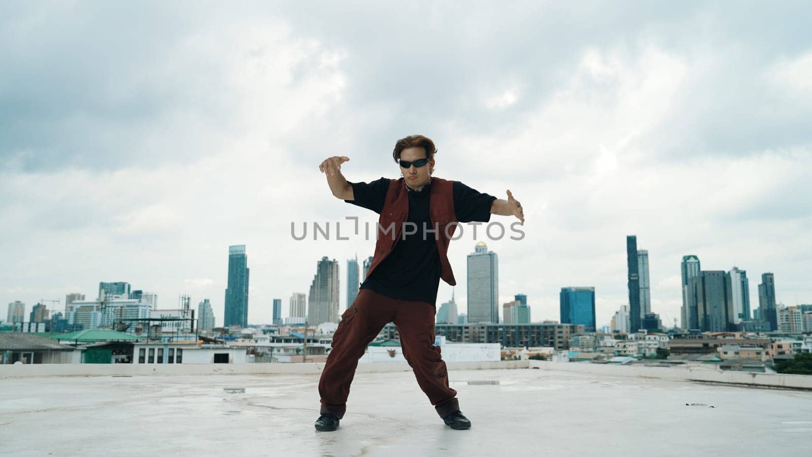 Motion shot of B-boy dance performance by professional street dancer at rooftop with sky scrapper, city view. Attractive asian hipster show energetic footstep. Outdoor sport 2024. Endeavor.