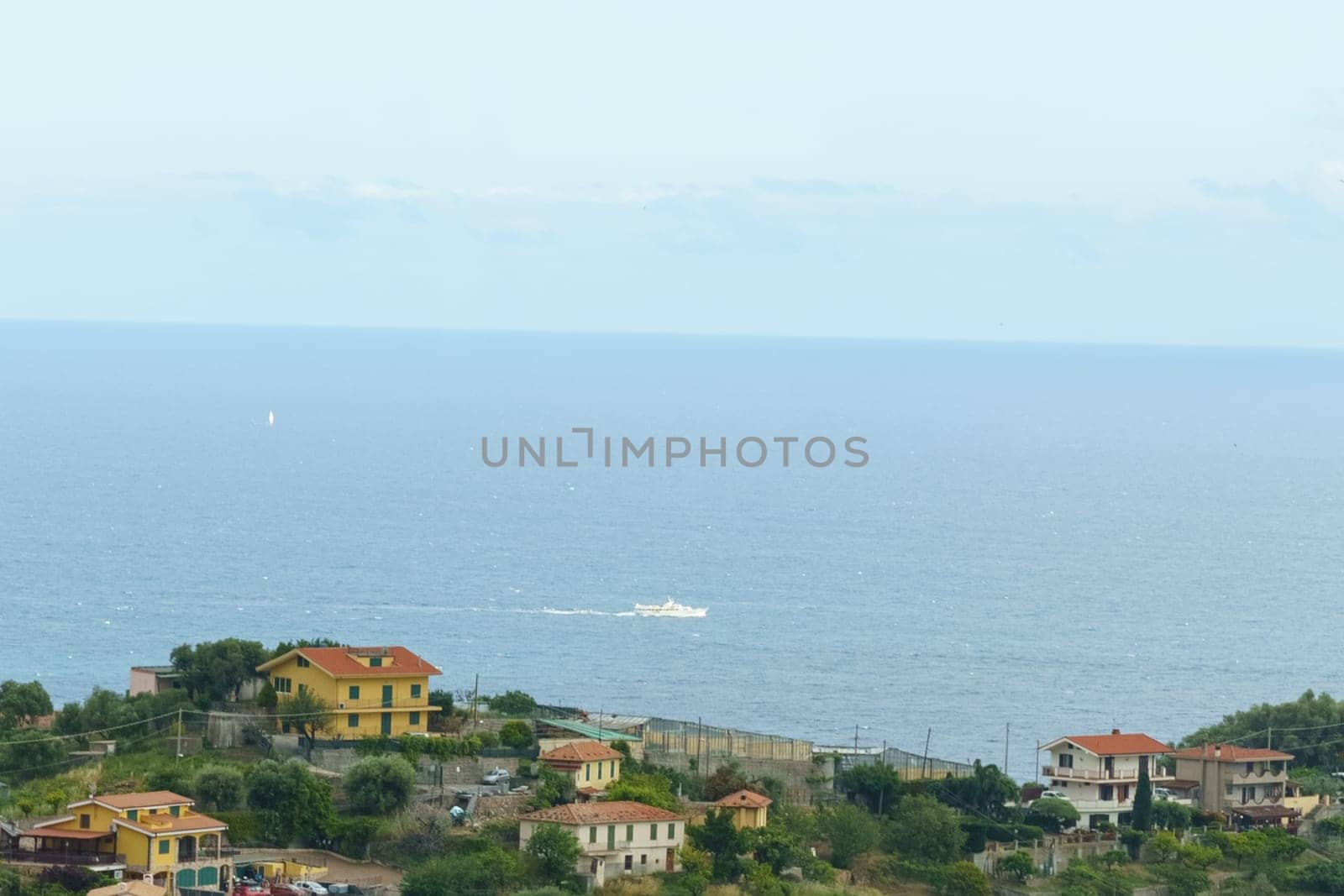 A view from a hill shows a body of water stretching into the distance, surrounded by lush greenery. The sunlight reflects off the water, creating a serene scene. Coast, Ligurian Sea