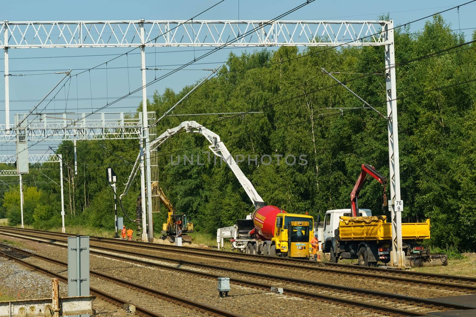 Kutno, Poland - June 16, 2023: Workers operating heavy machinery to maintain and repair railway tracks amidst lush greenery under a clear blue sky.