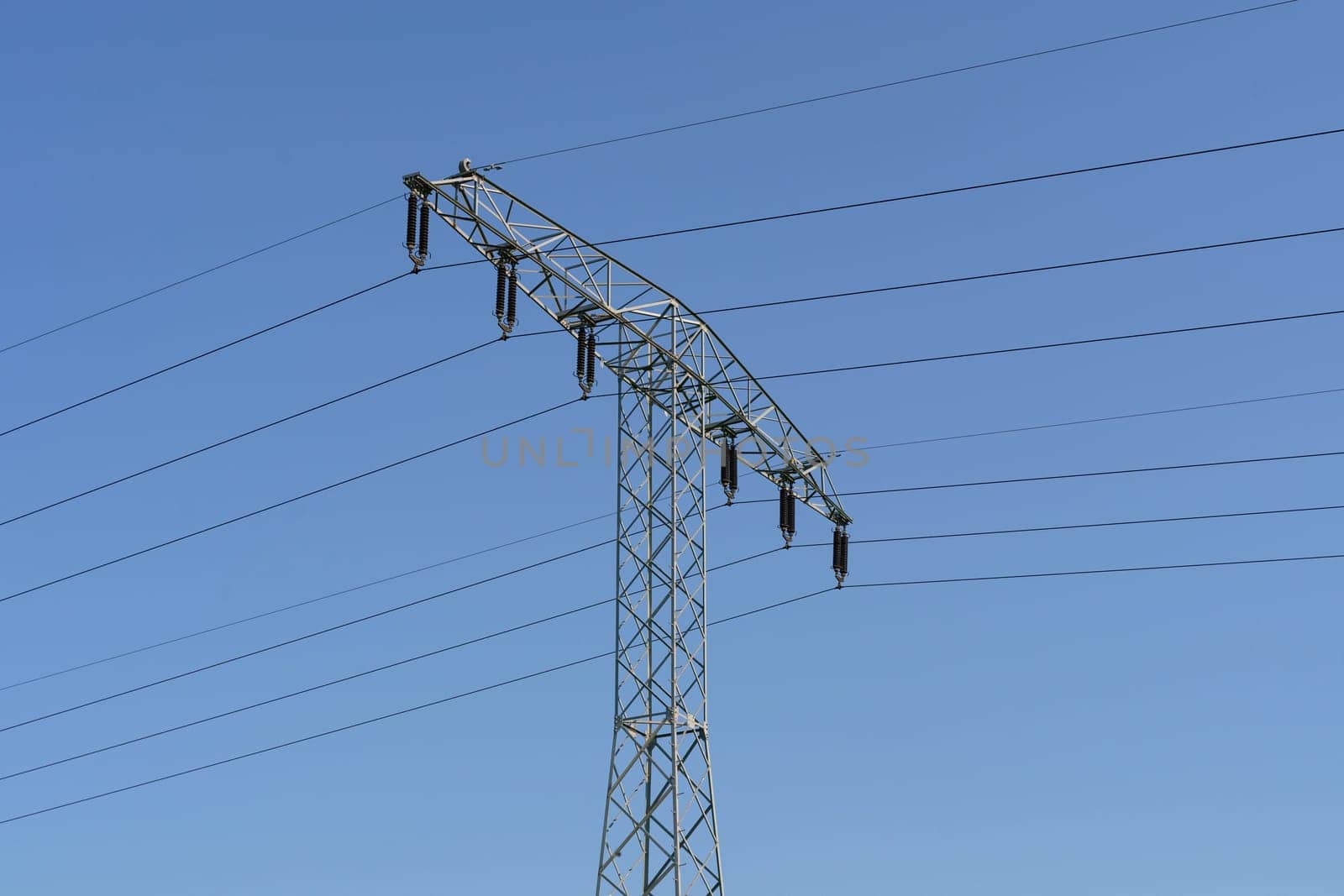 A high voltage power line towers against a clear blue sky, carrying electricity across the landscape.