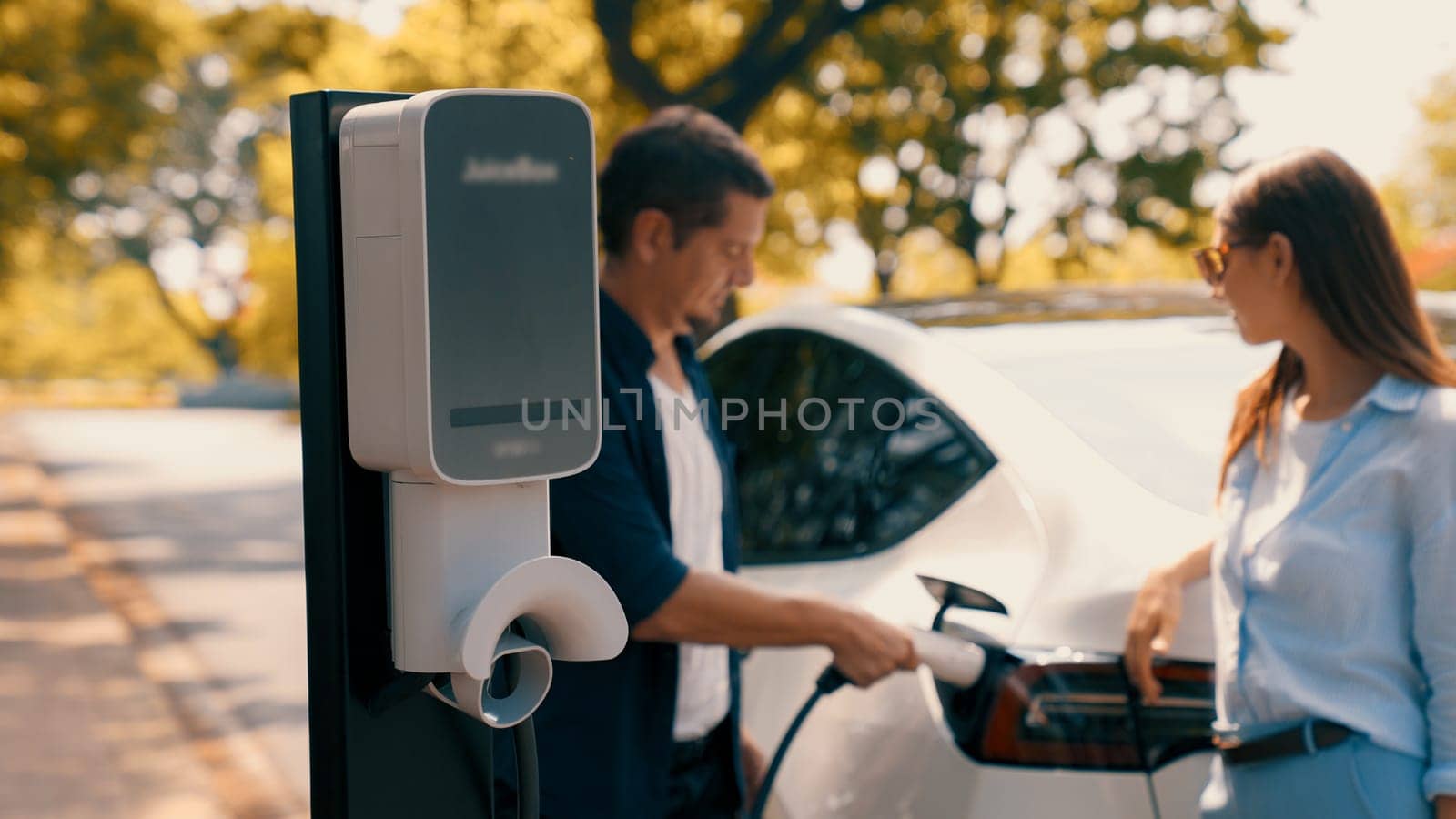 EV car recharging electricity for battery by lovey couple on road trip. Exalt by biancoblue
