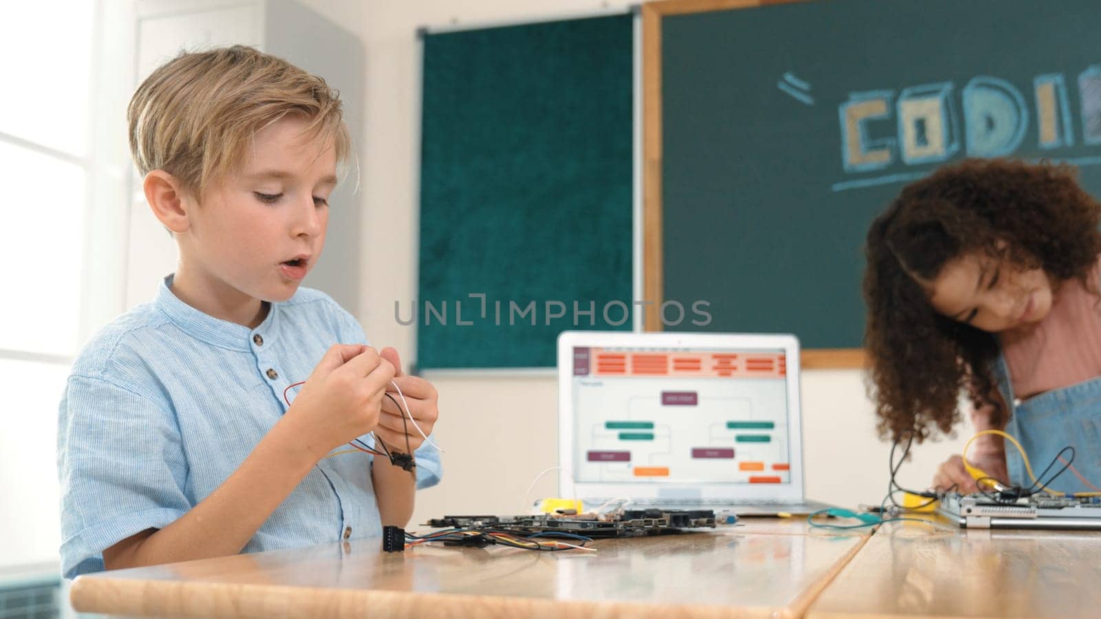 Girl standing while fixing electronic board by using screwdriver. American student and happy caucasian boy working together to inspect electric system. Curious children working on board. Pedagogy.