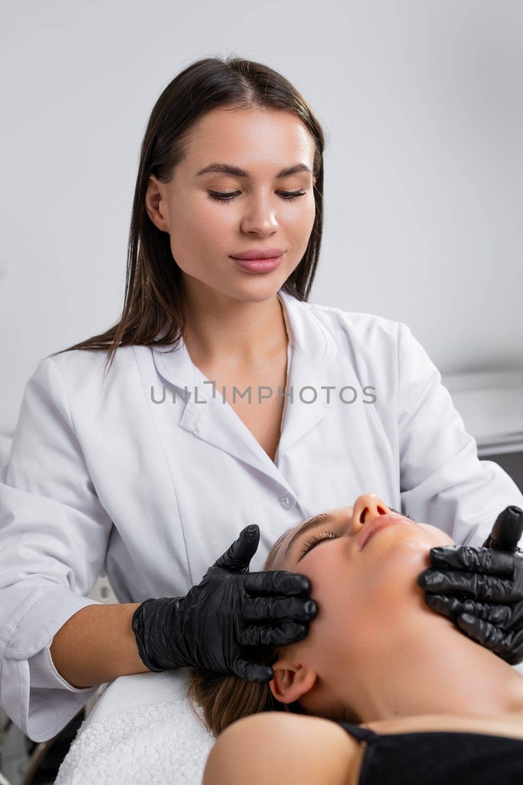 Young woman cosmetologist is doing facial treatment to lying young woman in a beauty spa salon.