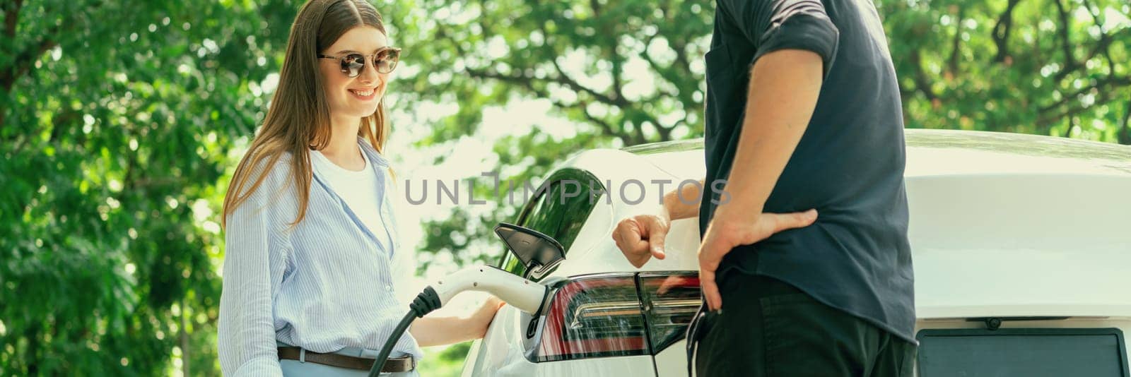 Focused EV car recharging electricity for battery on blurred couple. Exalt by biancoblue