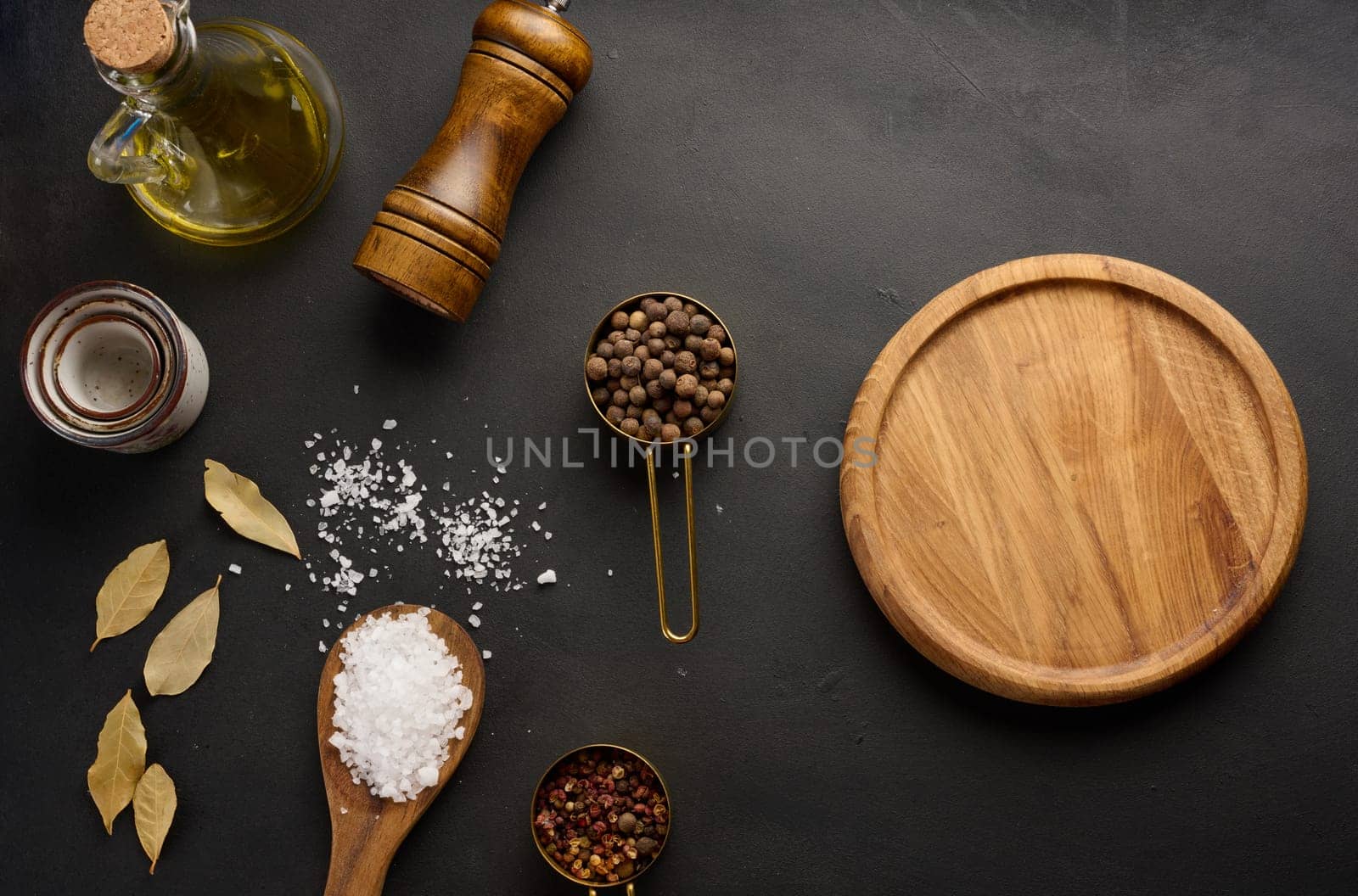 Salt, allspice, peppercorns and olive oil in a bottle on a black table by ndanko