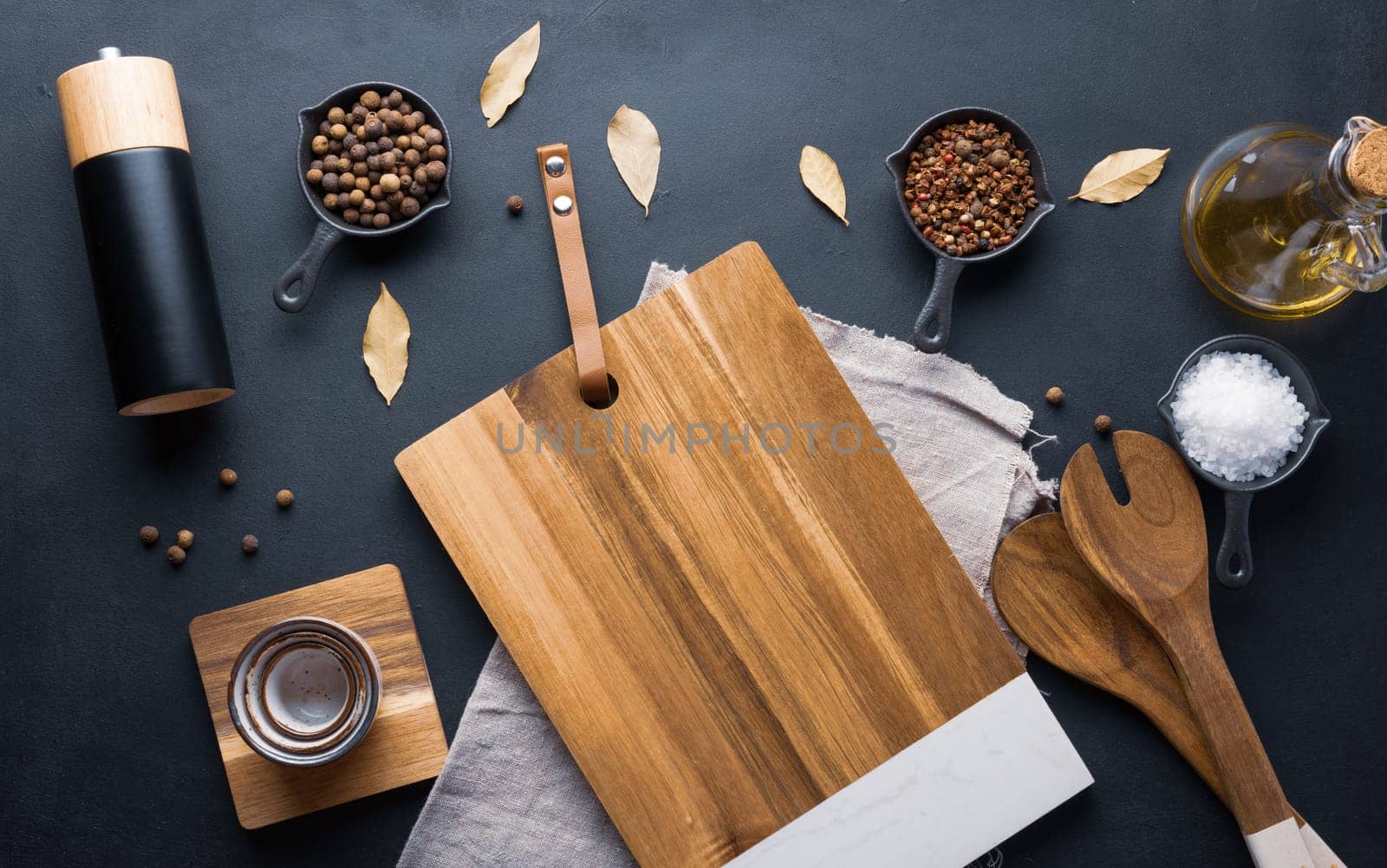 Empty wooden cutting board, salt, allspice, peppercorns and olive oil in a bottle on a black table by ndanko