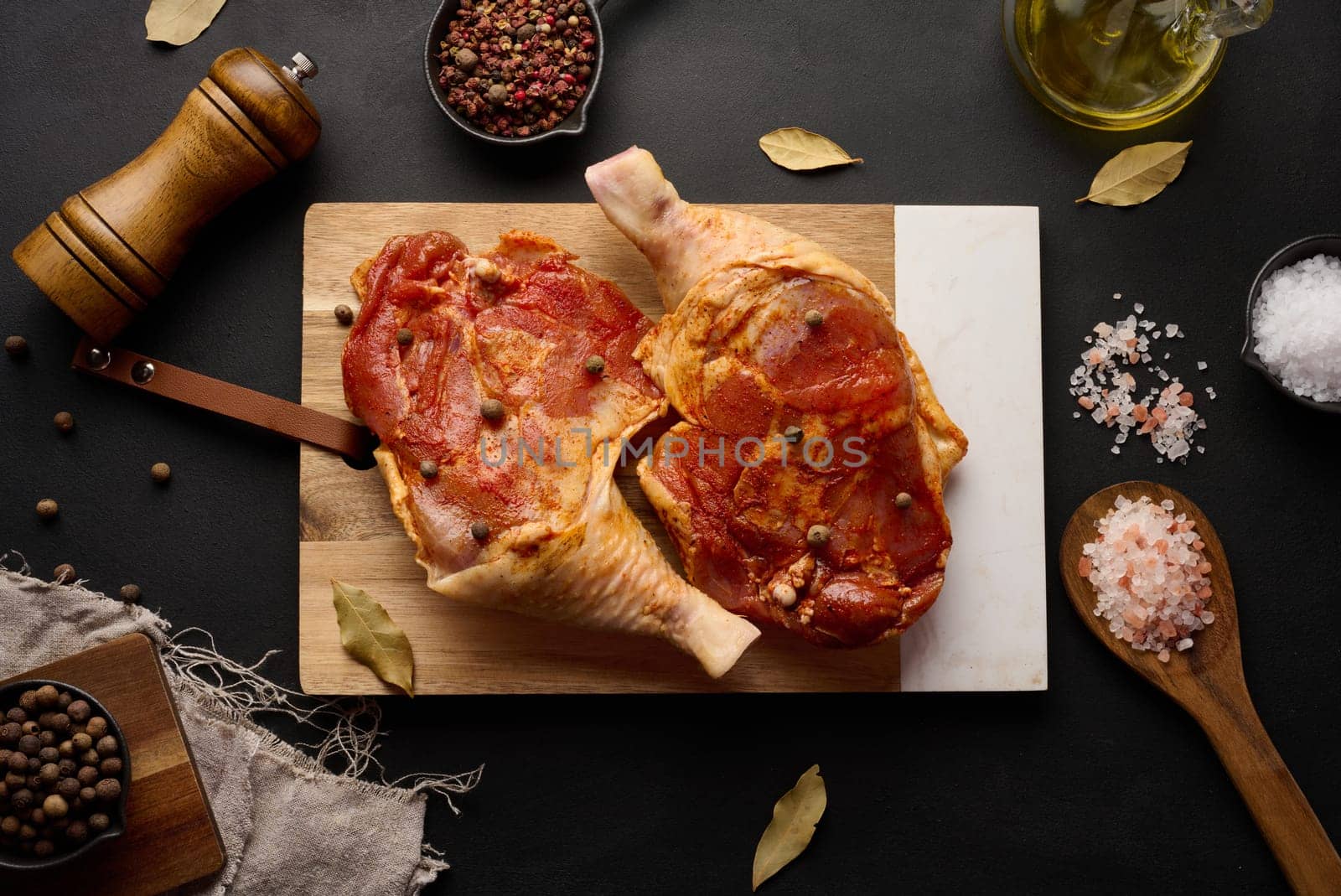 Raw chicken drumsticks seasoned on a wooden board, accompanied by salt and peppercorns, viewed from the top.  by ndanko