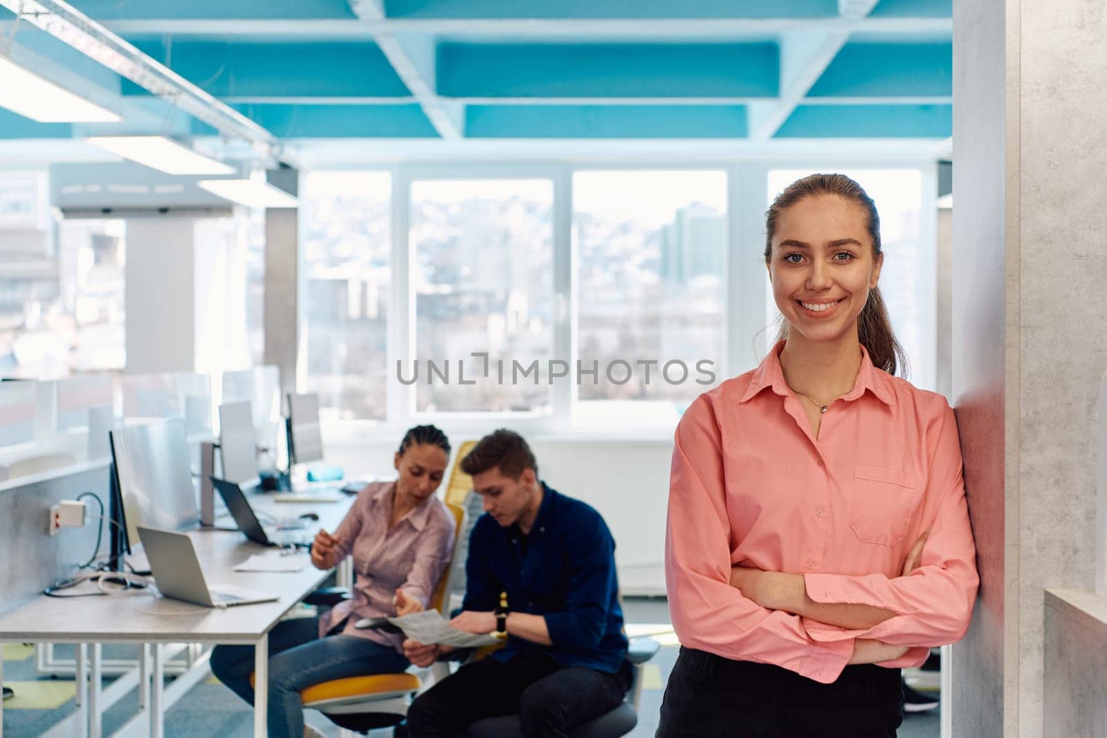 Portrait of young smiling business woman in creative open space coworking startup office. Successful businesswoman standing in office with copyspace. Coworkers working in background by dotshock