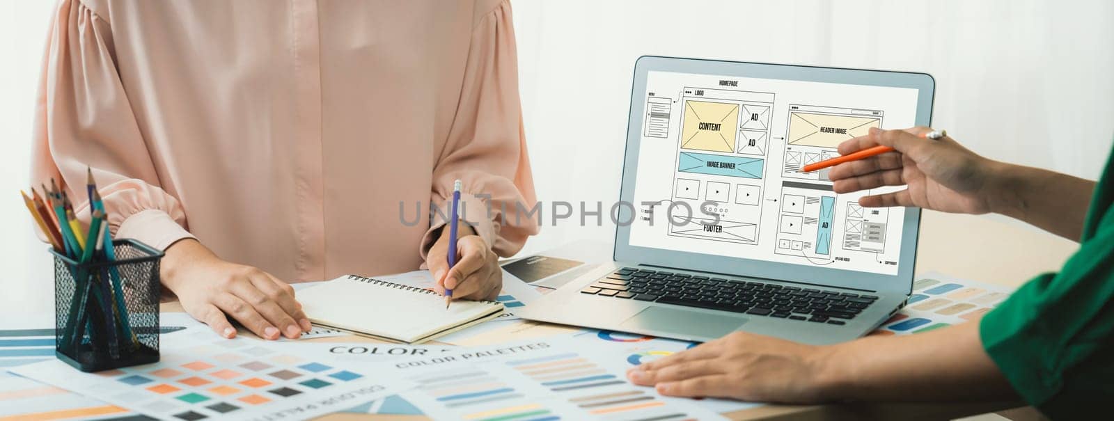 Cropped image of interior designer presents color from color swatches while laptop displayed website wireframe designs for mobiles app and website. Creative design and business concept. Variegated.