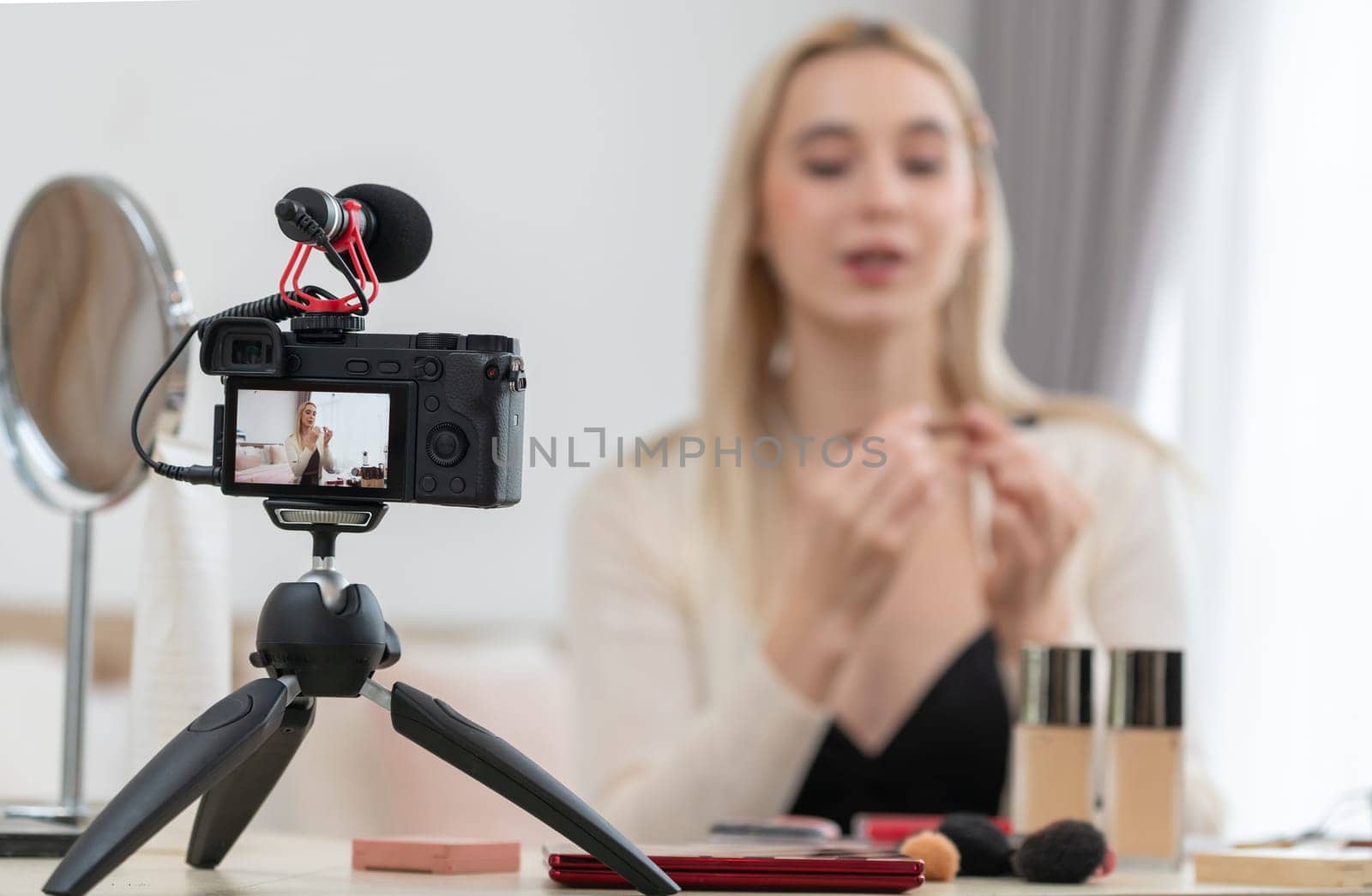 Blurred young woman making beauty and cosmetic tutorial video content for social media. Focused camera screen with beauty influencer showing how to apply beauty care to audience or followers. Blithe