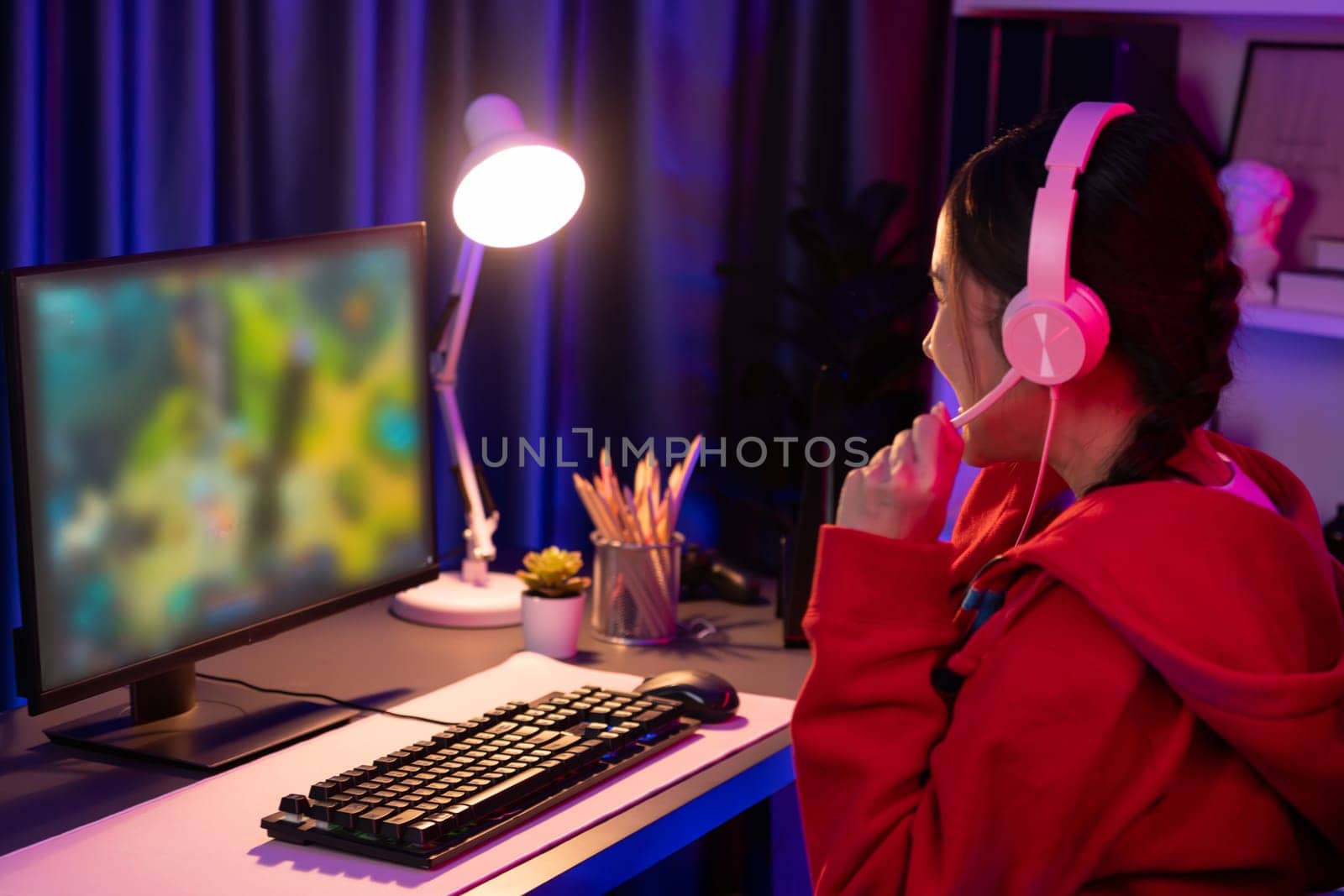 Host channel of young beautiful Asian gaming streamer playing fighting Moba at battle arena game on pc screen with multiplays, wearing pastel headphone at neon digital light modern room. Stratagem.